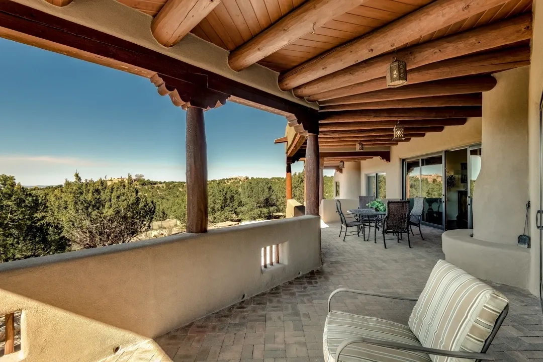 Cozy porch with wooden beams overlooking a scenic forest under a clear blue sky.