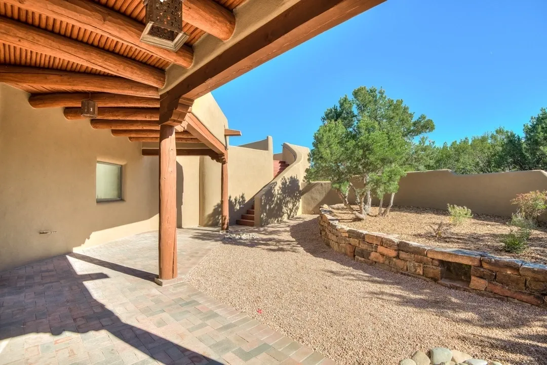 A sunny backyard with adobe-style walls and a wooden pergola.