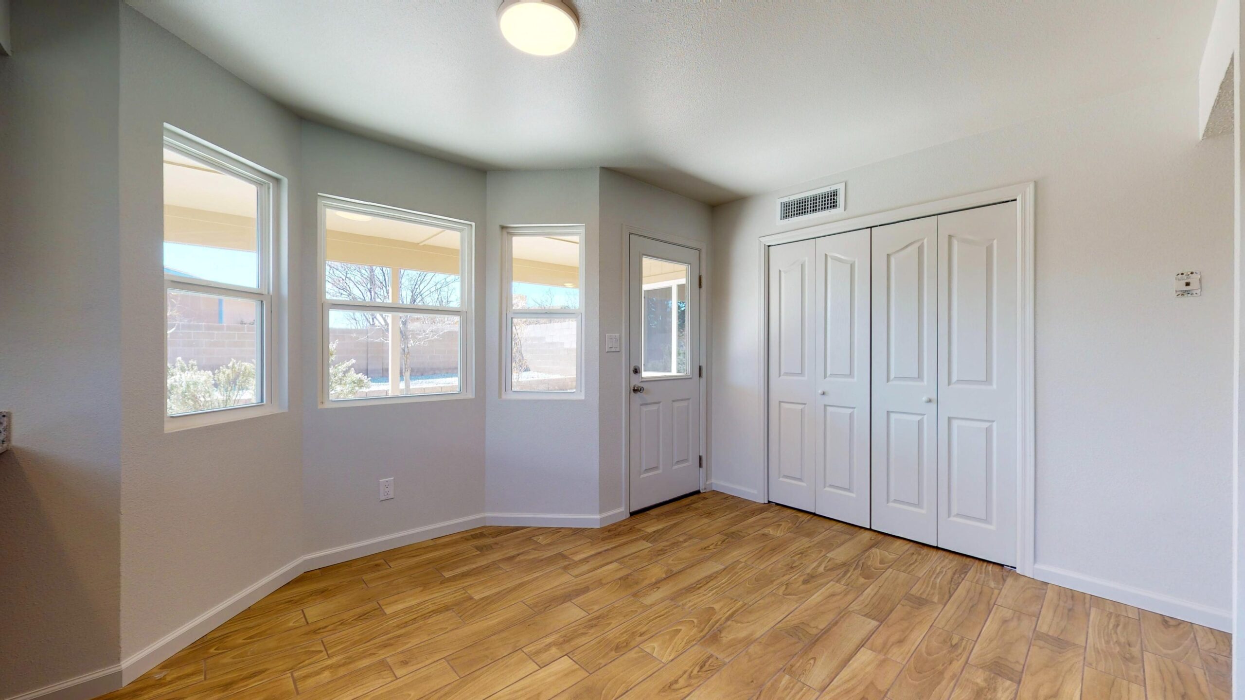 Bright empty room with large windows and wooden floor.