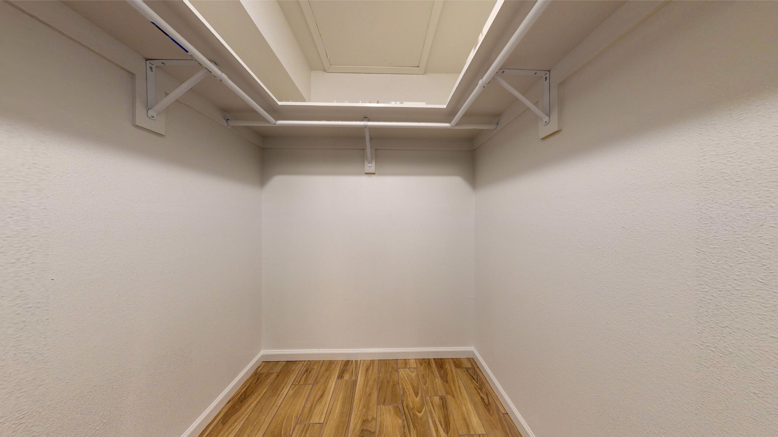 Empty closet with white walls and wooden floor.