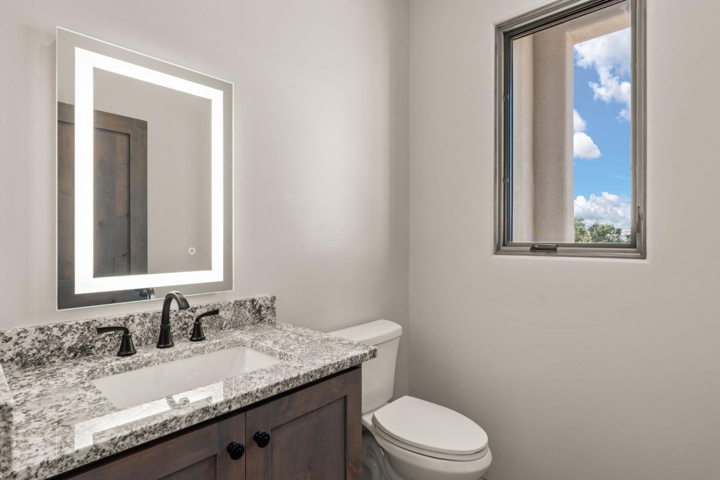 Modern bathroom with marble countertop and illuminated mirror.