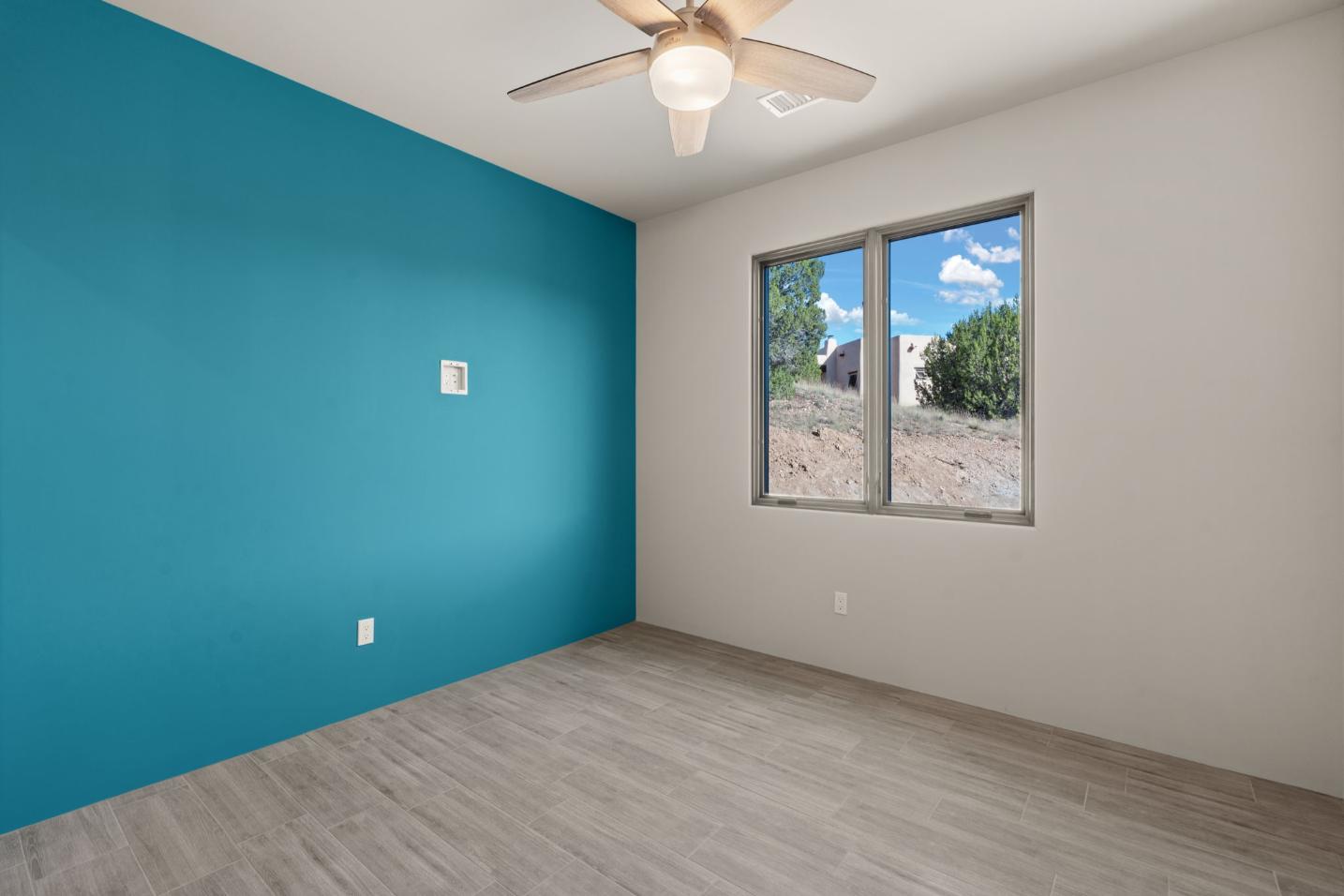 Bright, empty room with teal accent wall and window overlooking a sunny backyard.
