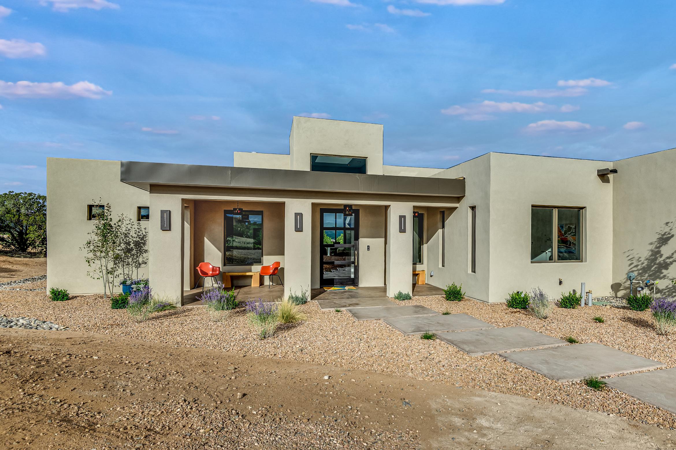 Modern stucco house with a flat roof and desert landscaping under a clear sky.