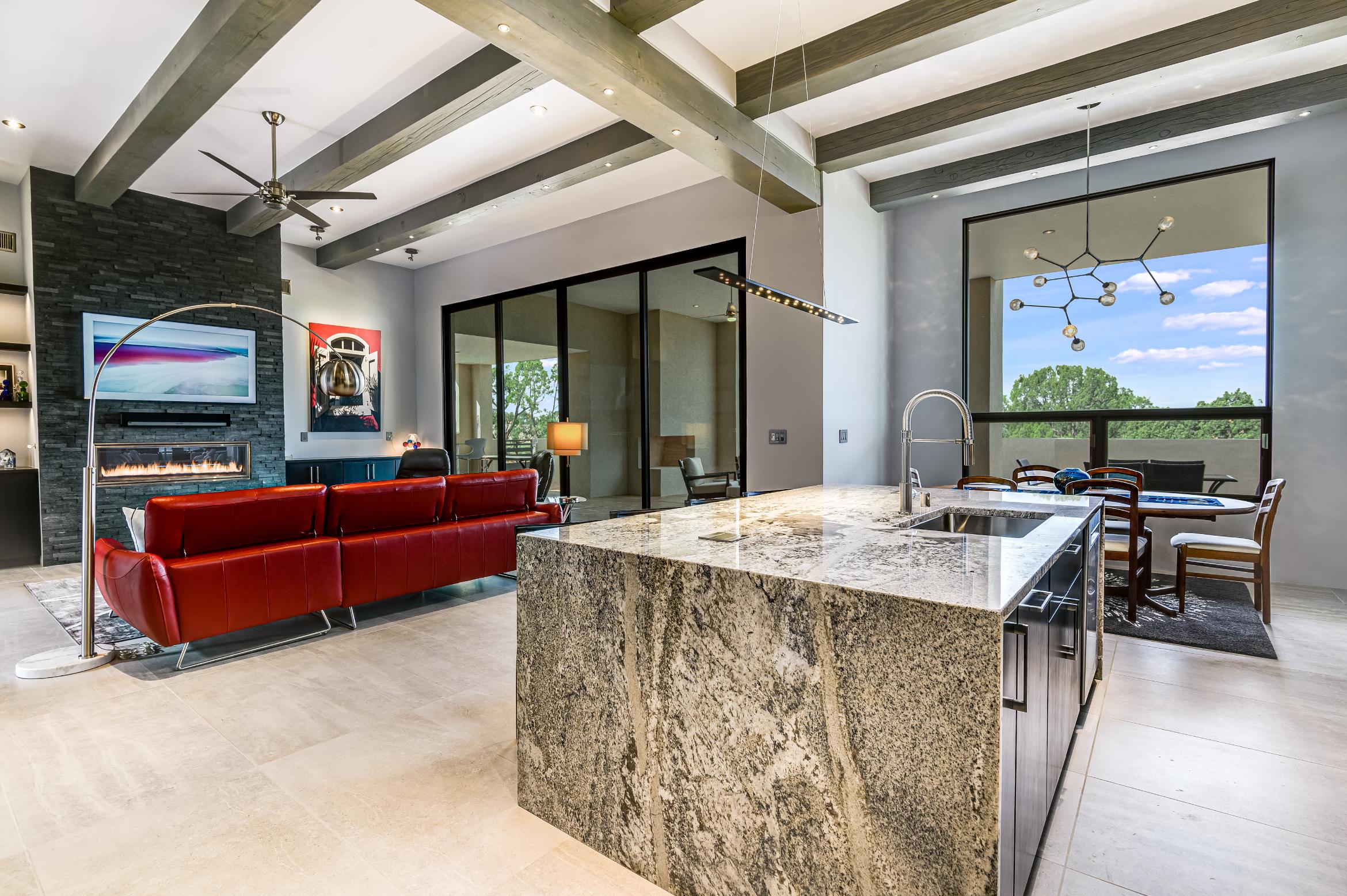 Modern kitchen with a large stone island and cozy living area in the background.