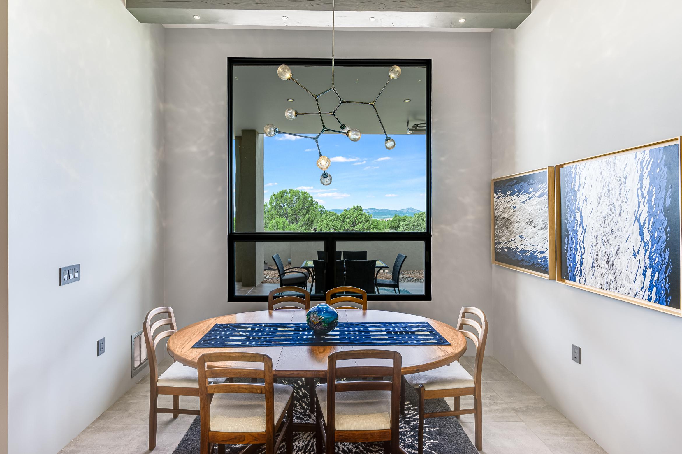 Modern dining room with a wooden table, chairs, and large window showing greenery.