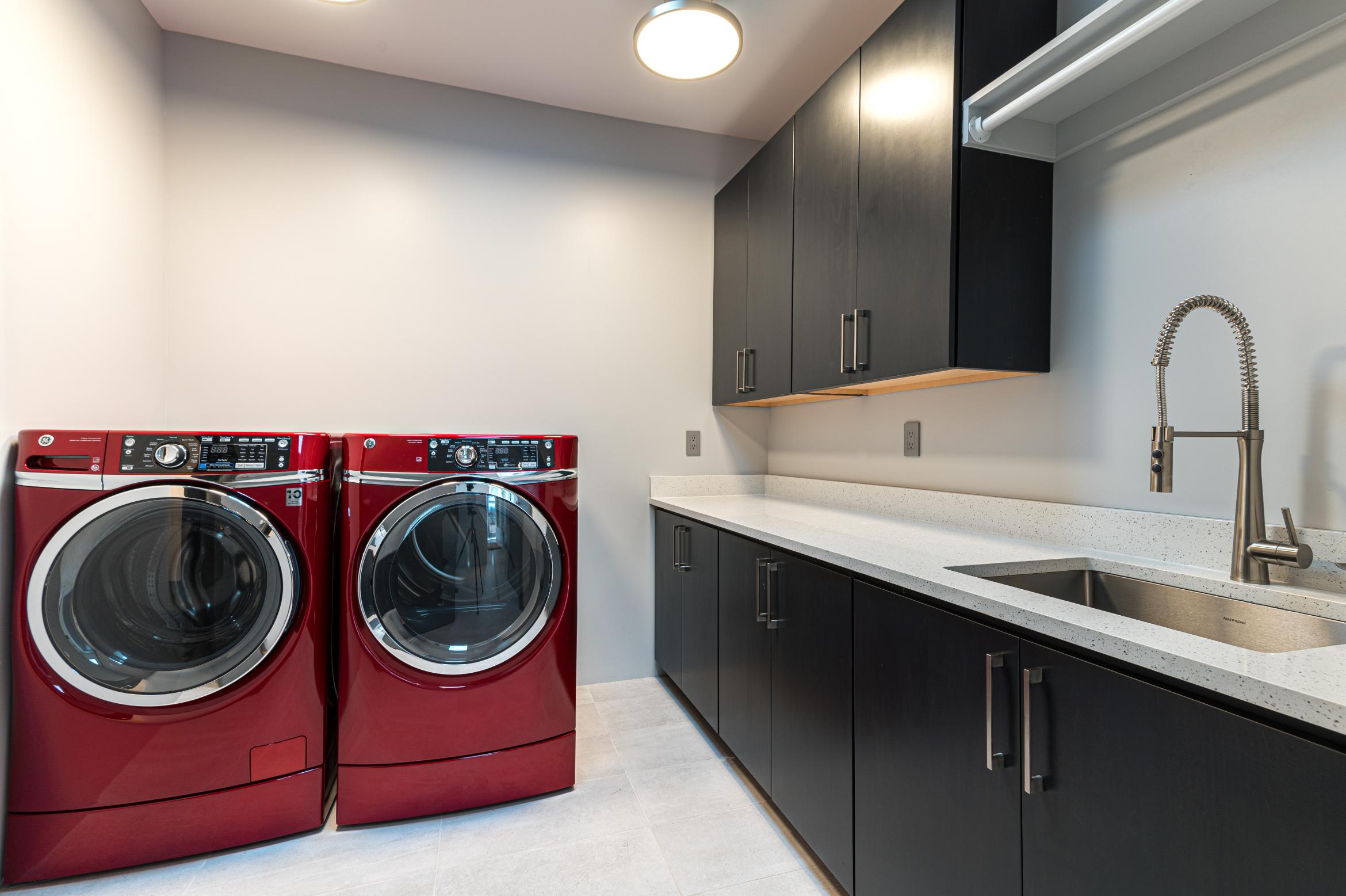 Modern laundry room with red washer and dryer and black cabinetry.