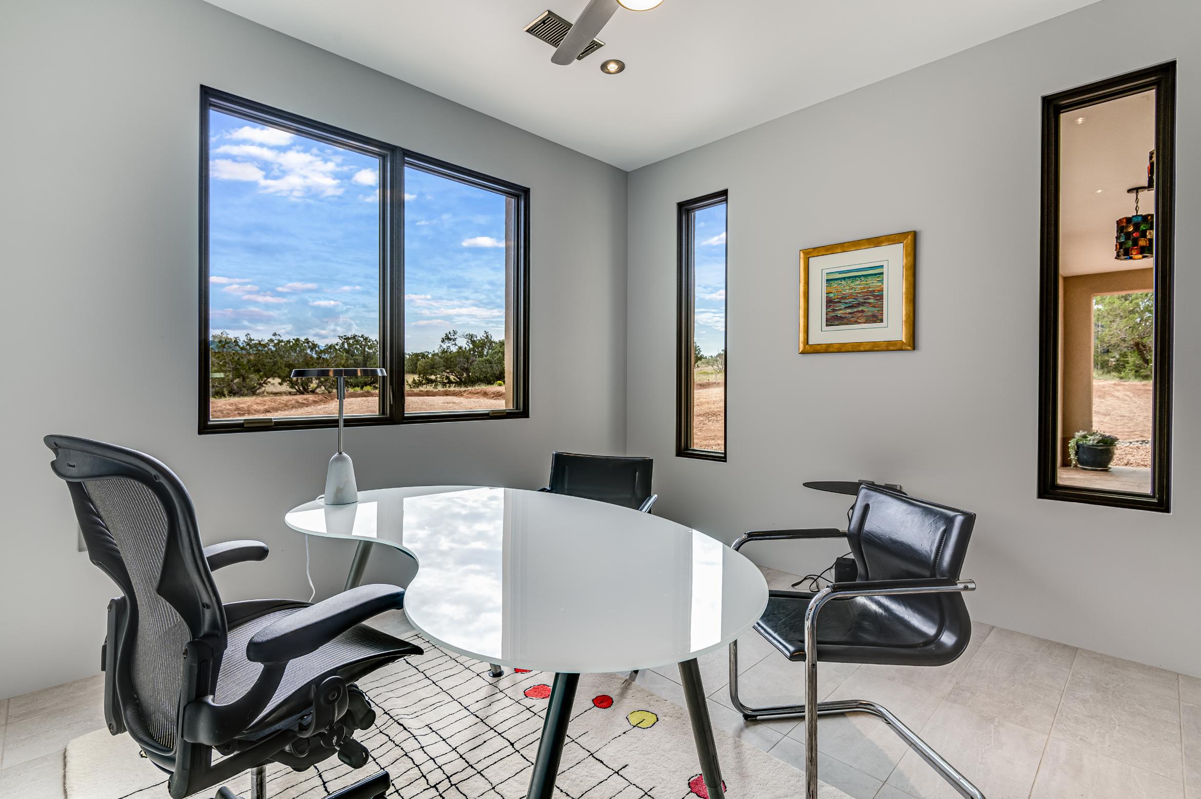 Modern office space with a round white table and black chairs near large windows.