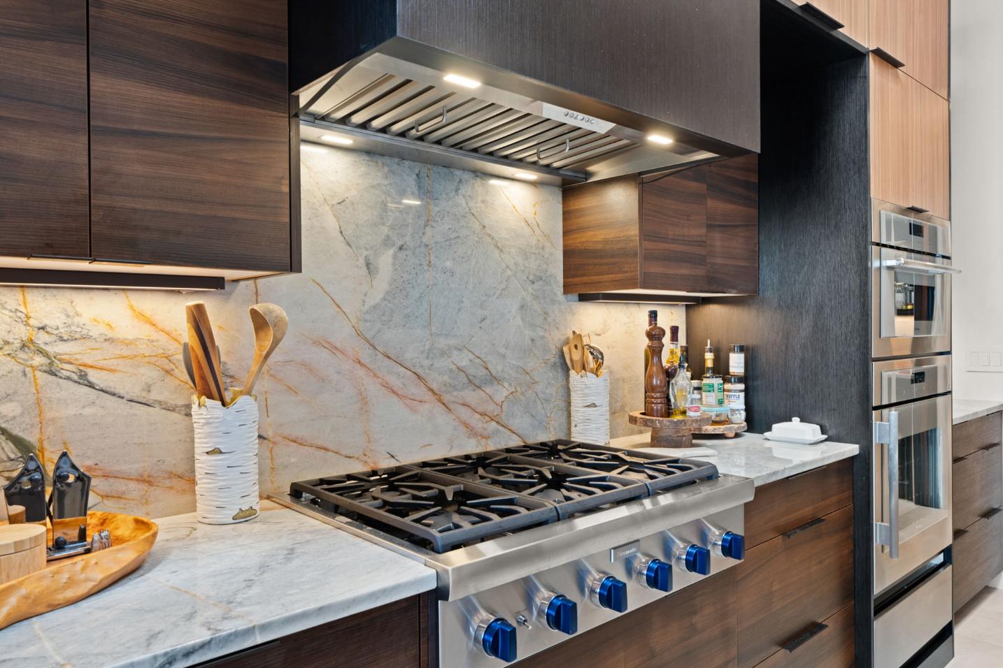 Modern kitchen stovetop with marble backsplash and wooden utensils.