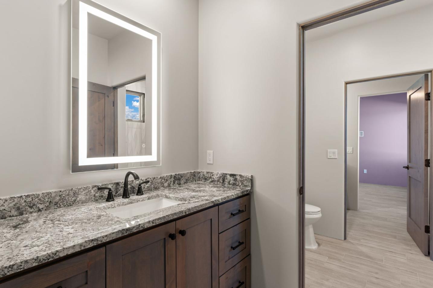 Modern bathroom with granite countertop and illuminated mirror.