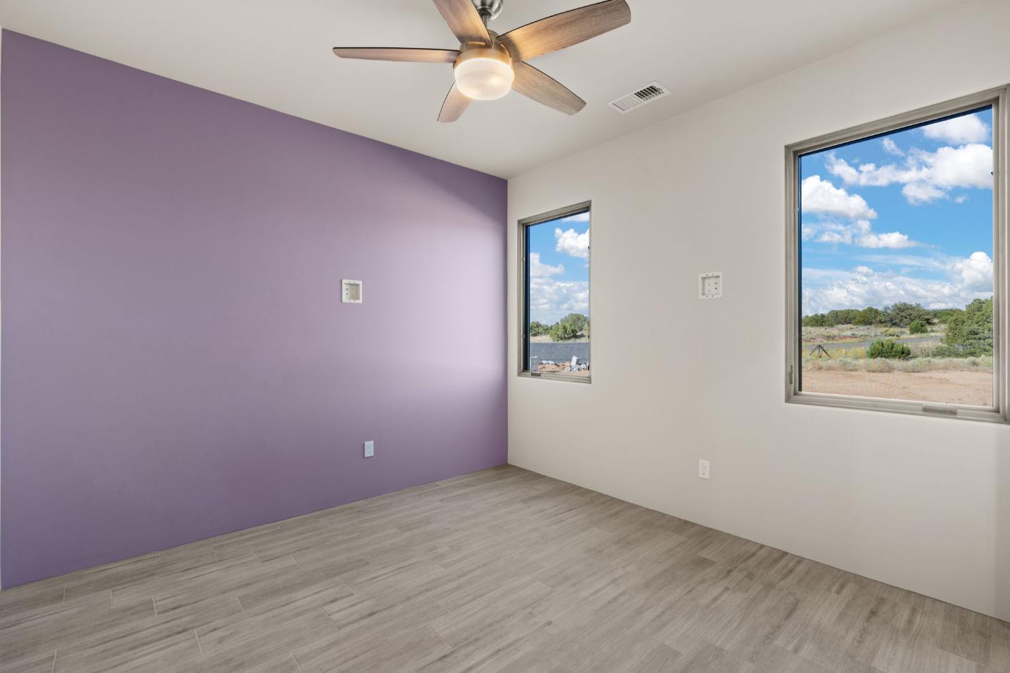 Empty room with purple accent wall and ceiling fan.