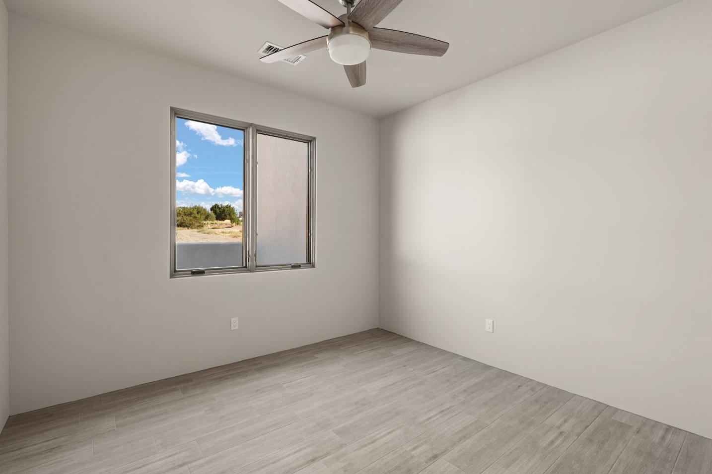 Empty room with window showing blue sky and ceiling fan.