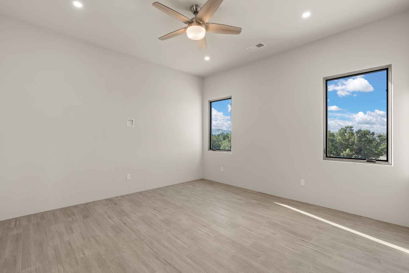 Bright, empty room with two windows and light wood flooring.