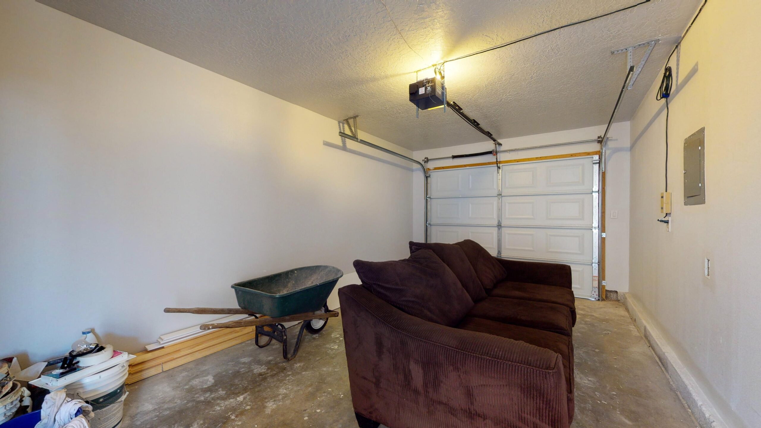 A purple couch and a wheelbarrow in a garage with a closed garage door.