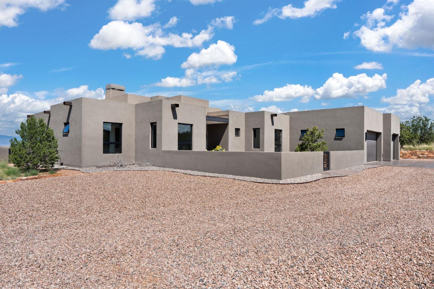 Modern adobe-style house under blue sky with gravel yard.