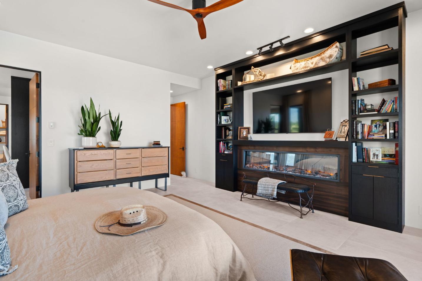 Modern bedroom with wooden ceiling fan and large TV on dark wood entertainment unit.