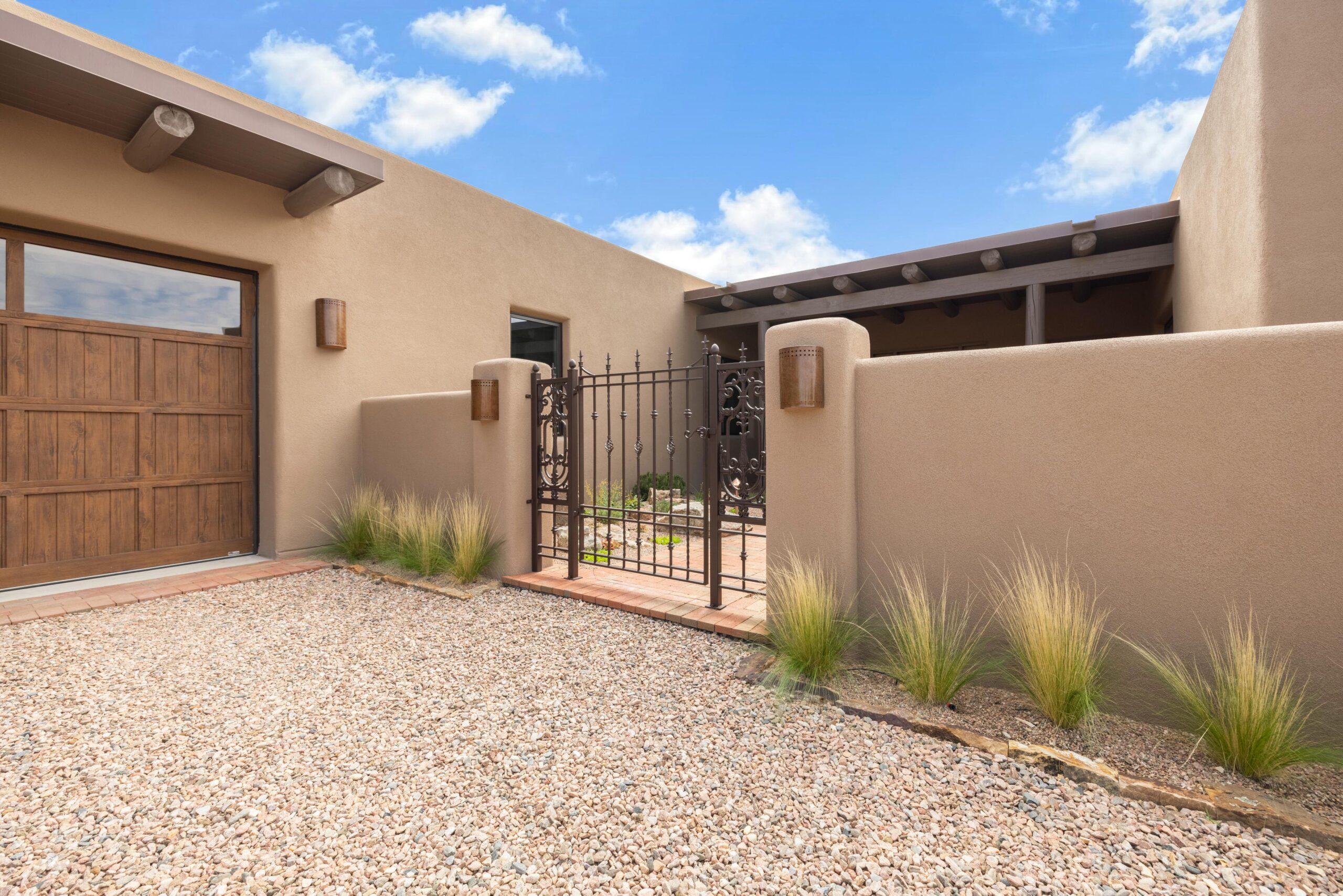Modern beige stucco home entrance with metal gate and desert landscaping.