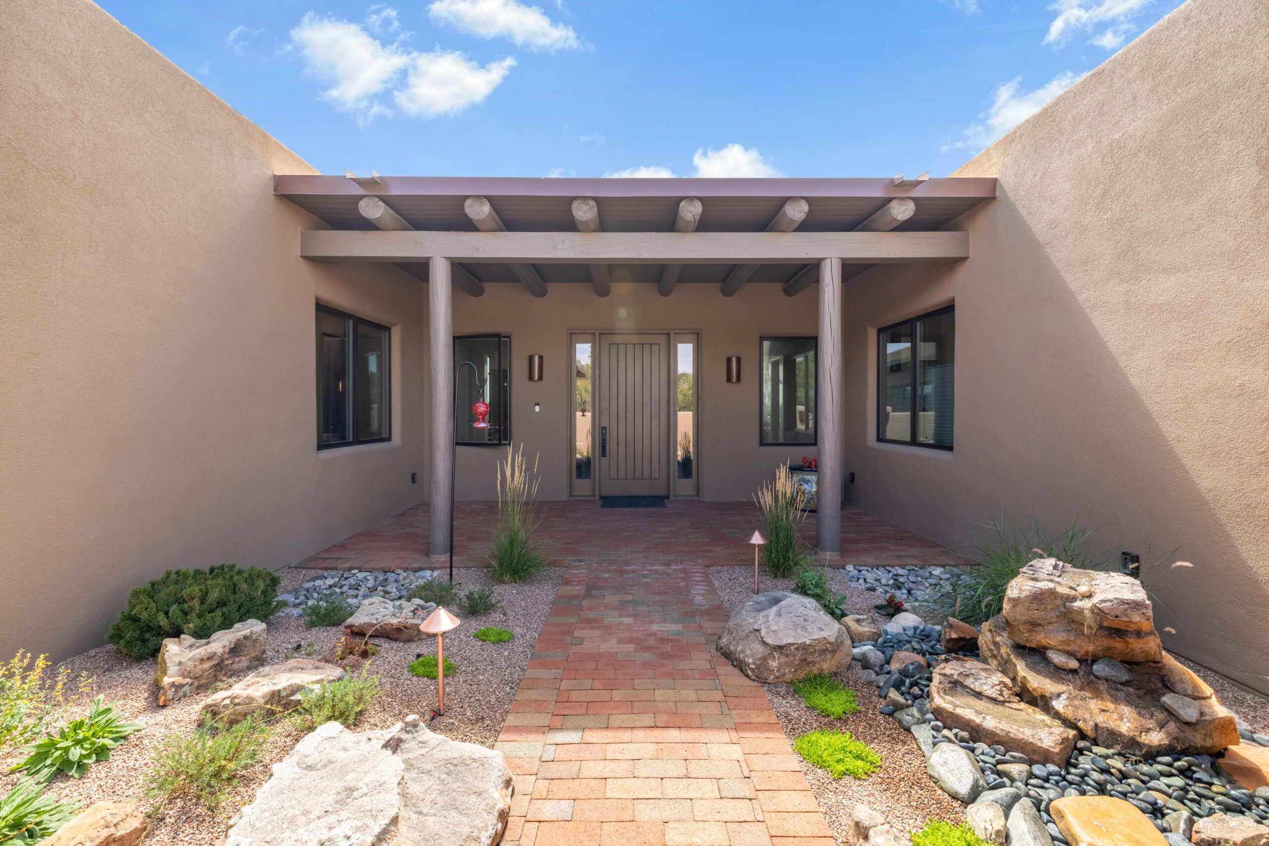 Spanish-style house entrance with pergola and brick pathway.
