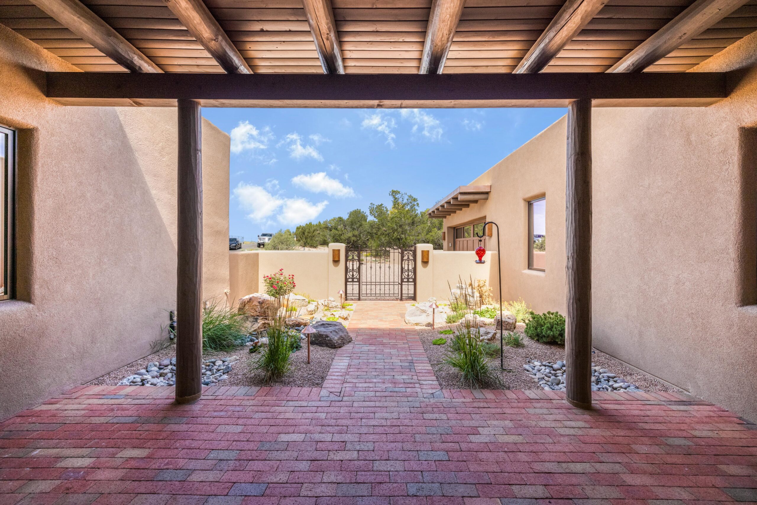 Sunny courtyard with brick flooring and adobe-style walls under a wooden pergola.
