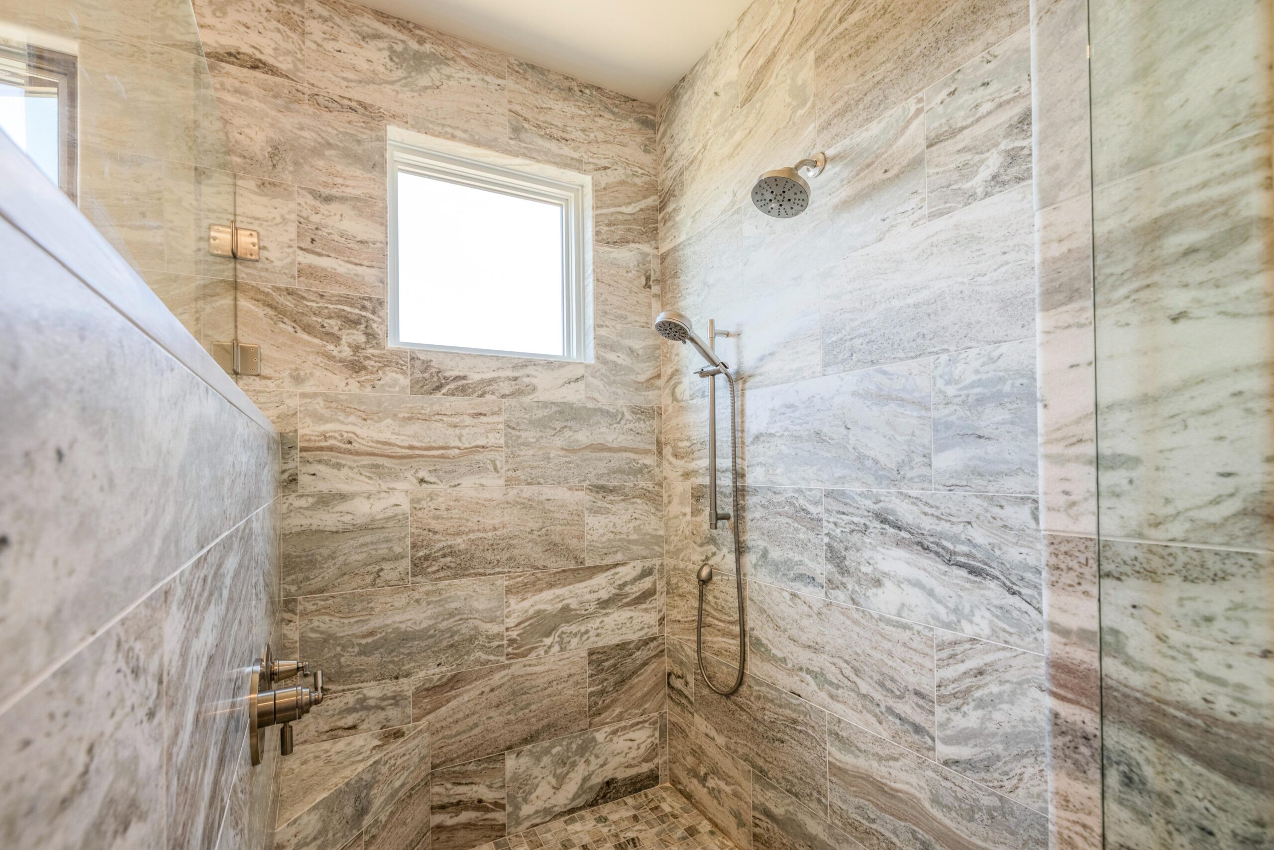 Modern shower with marble walls and a rain showerhead under a window.