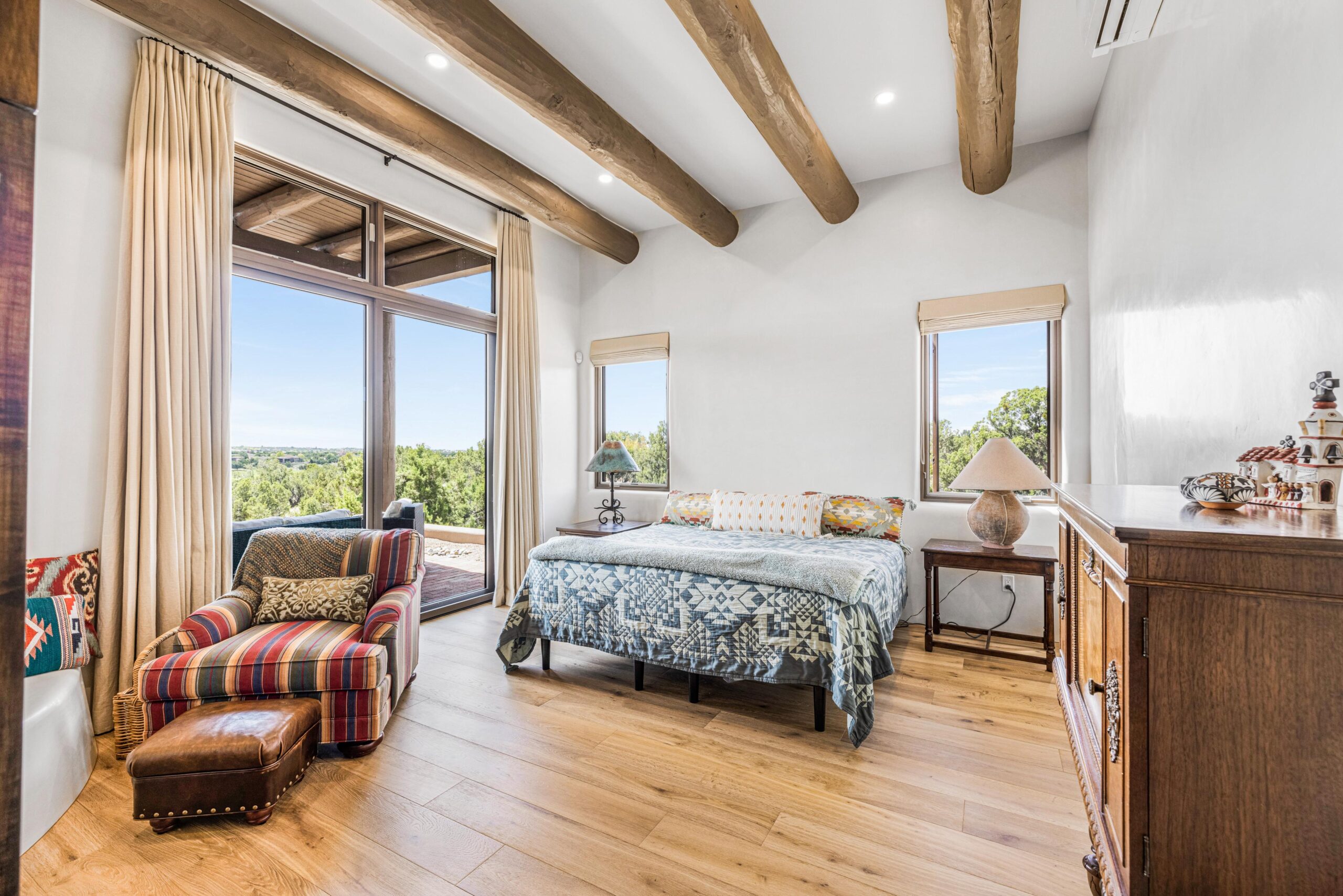 Bright bedroom with wooden beams and large windows overlooking greenery.