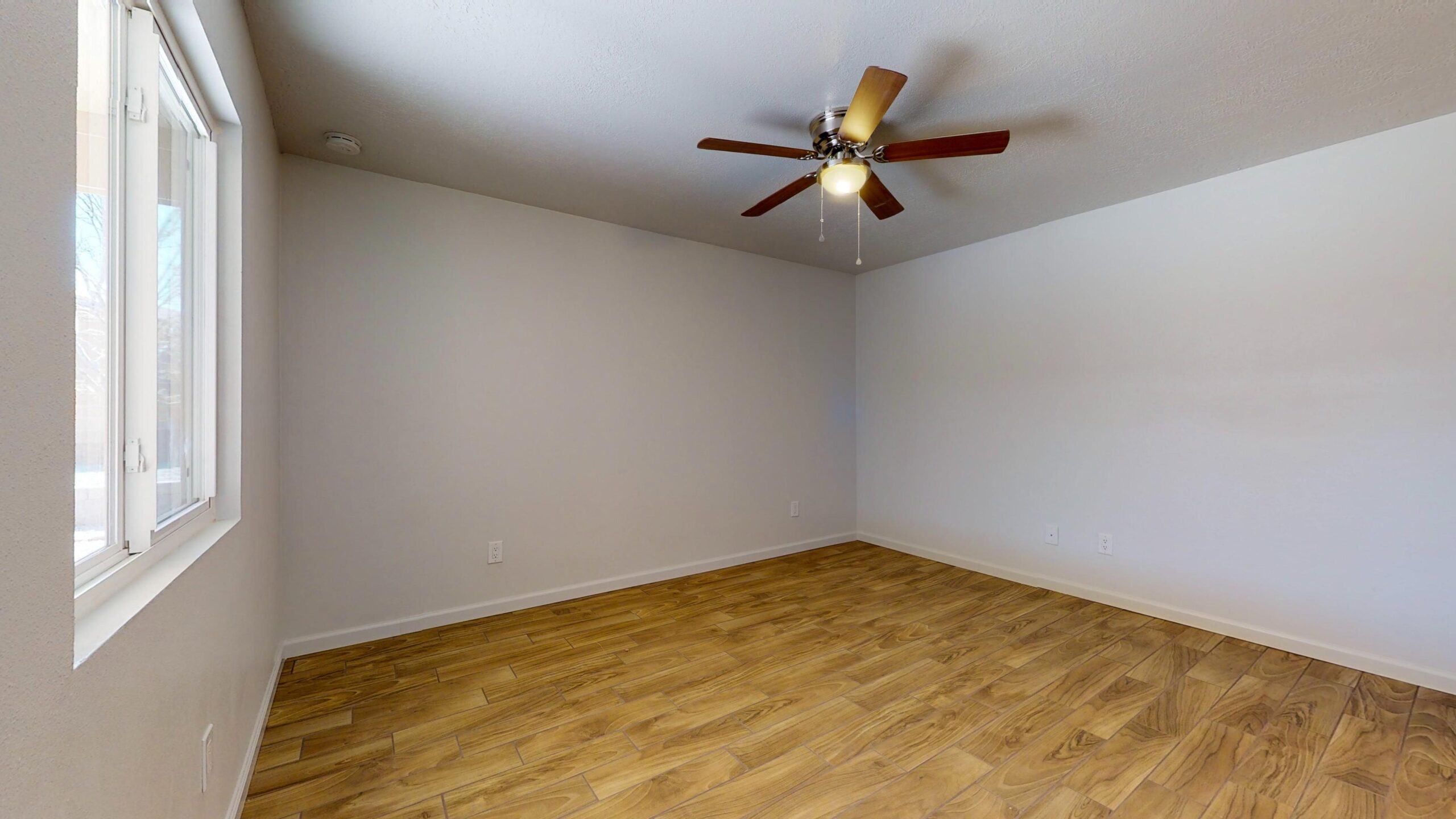 Empty room with wood flooring and ceiling fan.