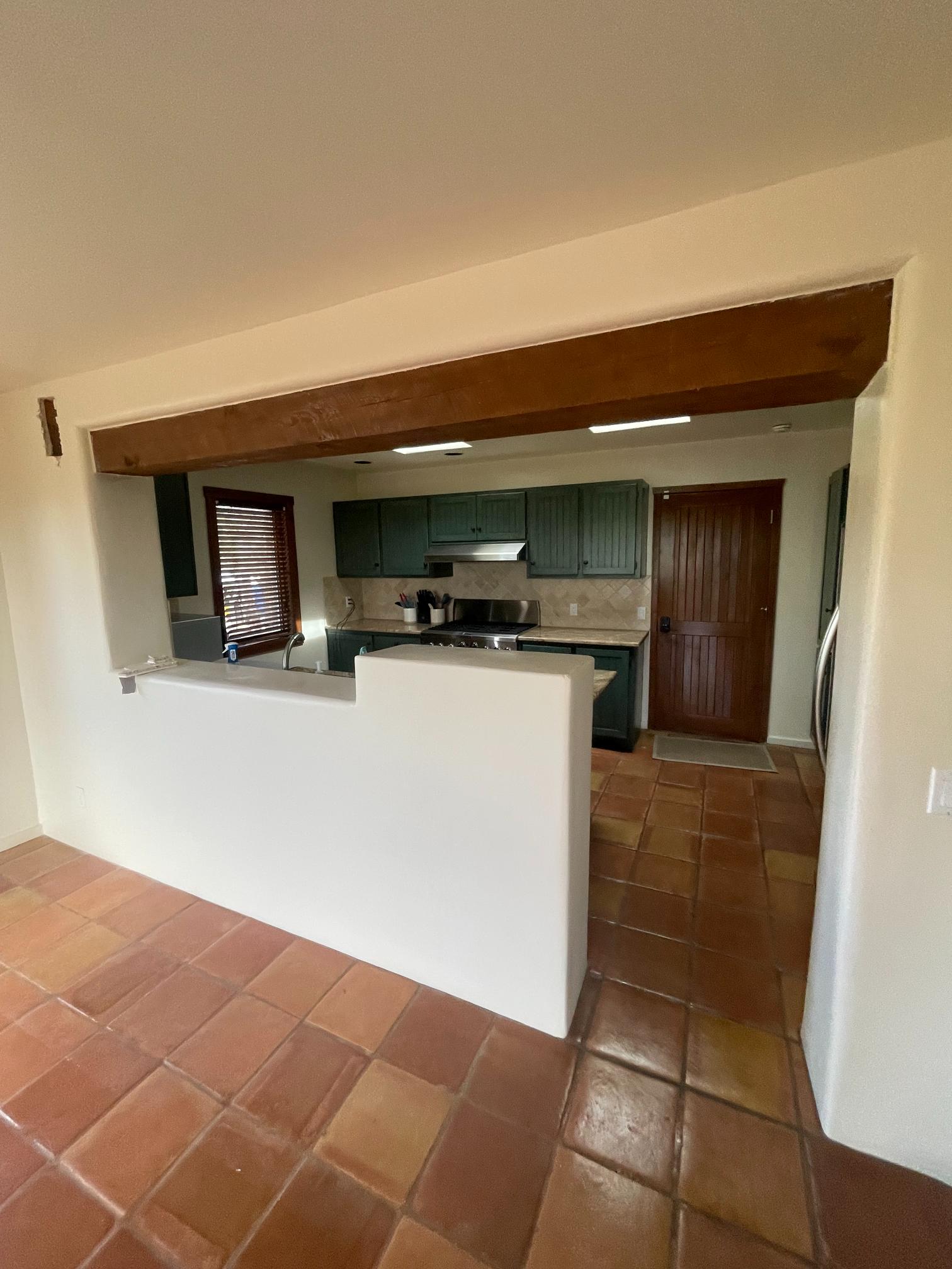 Open kitchen with green cabinets and a wooden beam.