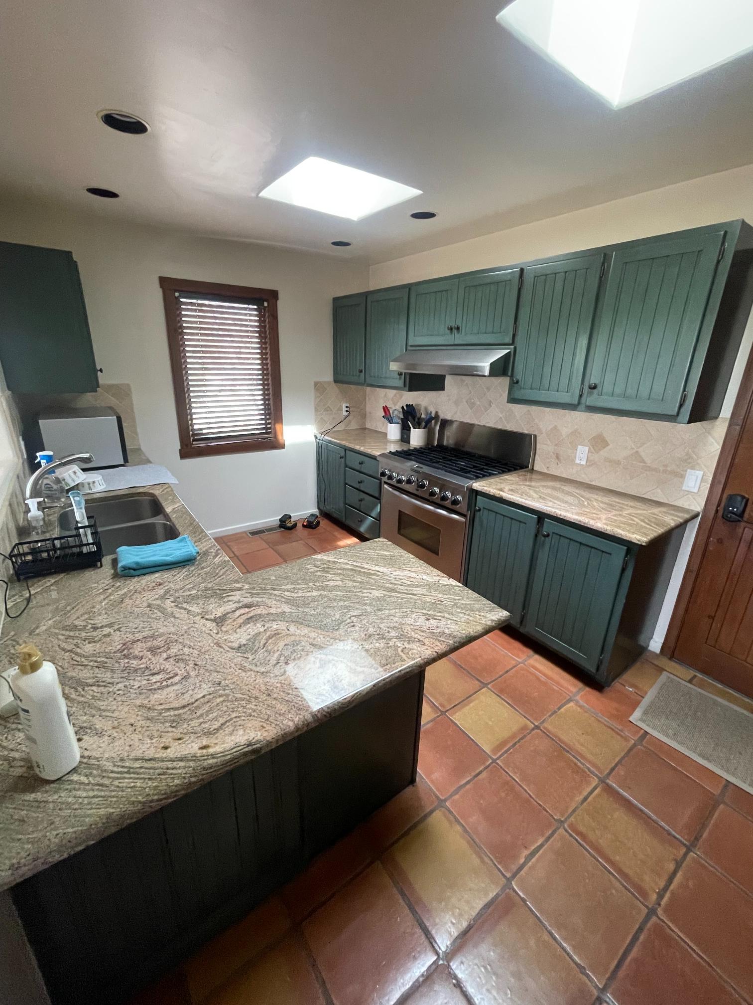 Spacious kitchen with green cabinets and granite countertops.