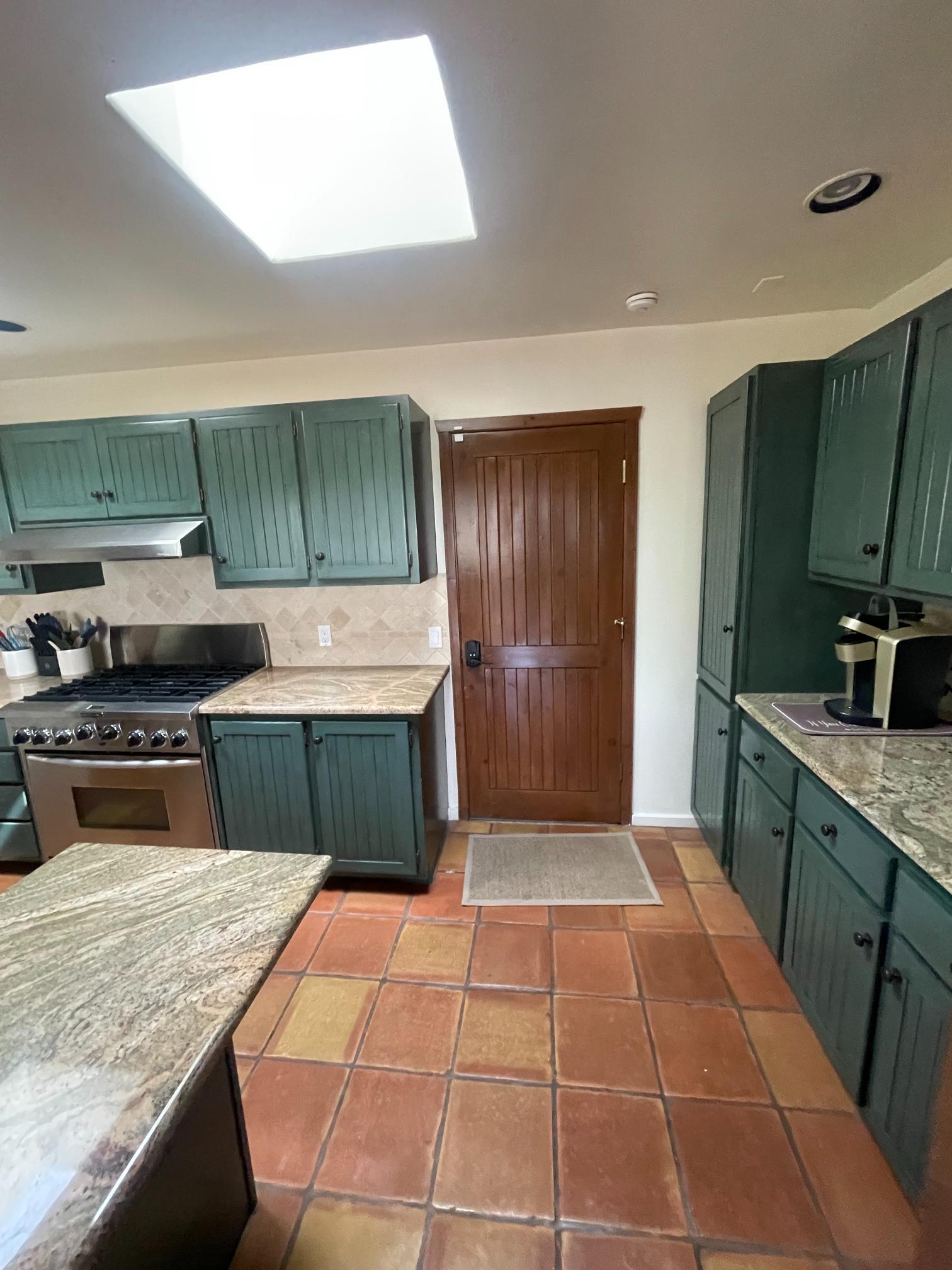 Cozy kitchen with green cabinets and terracotta tile floor.