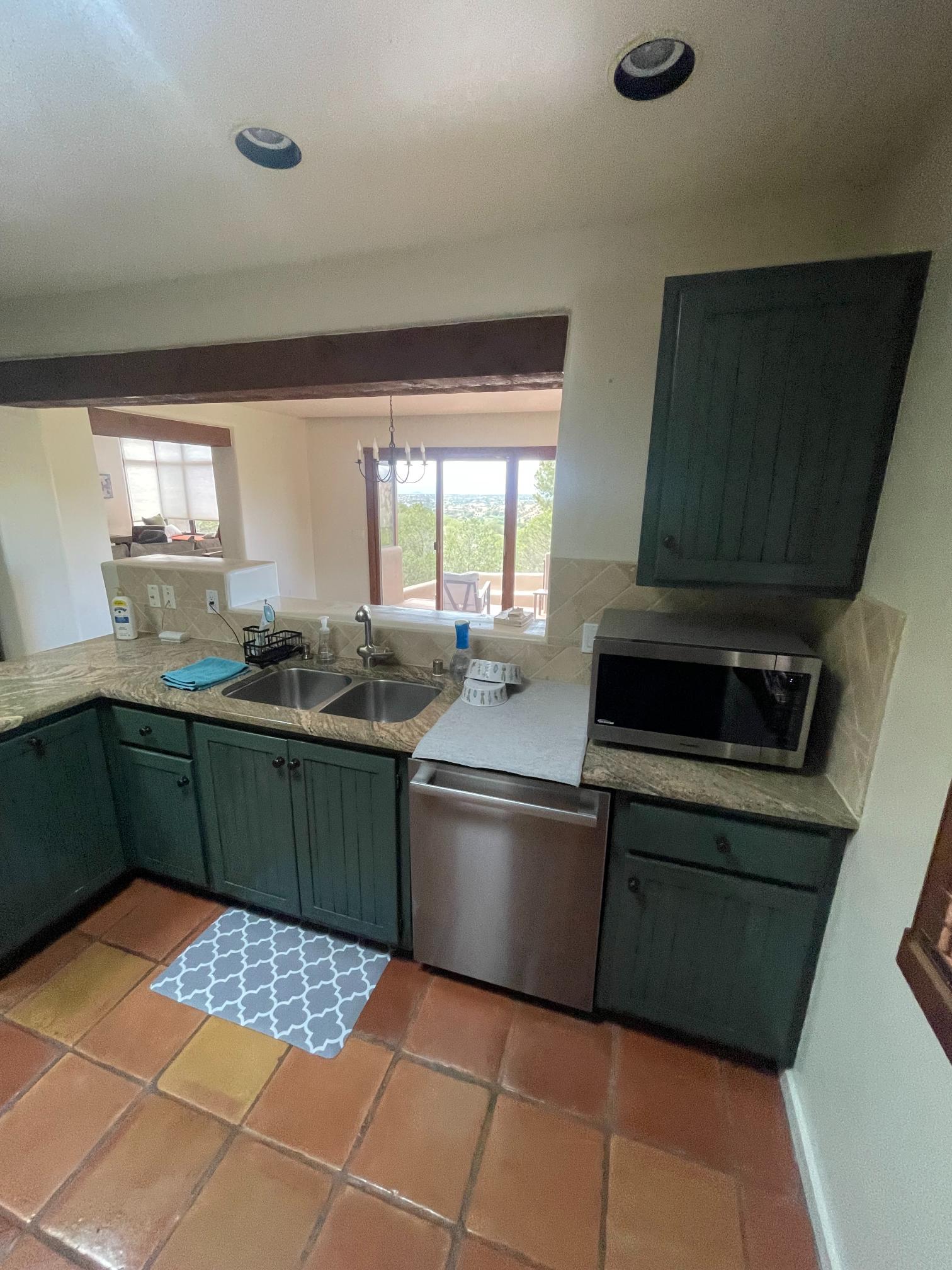 Cozy kitchen with green cabinets, microwave, and window view.