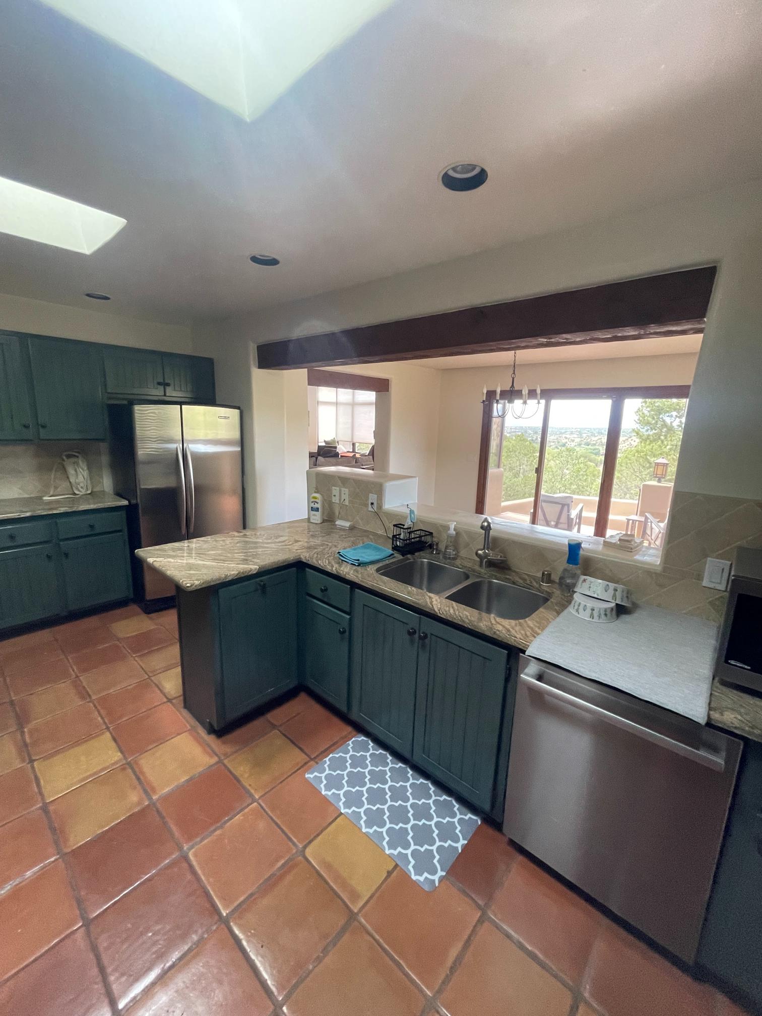 Modern kitchen with green cabinets, stainless steel appliances, and a large window.