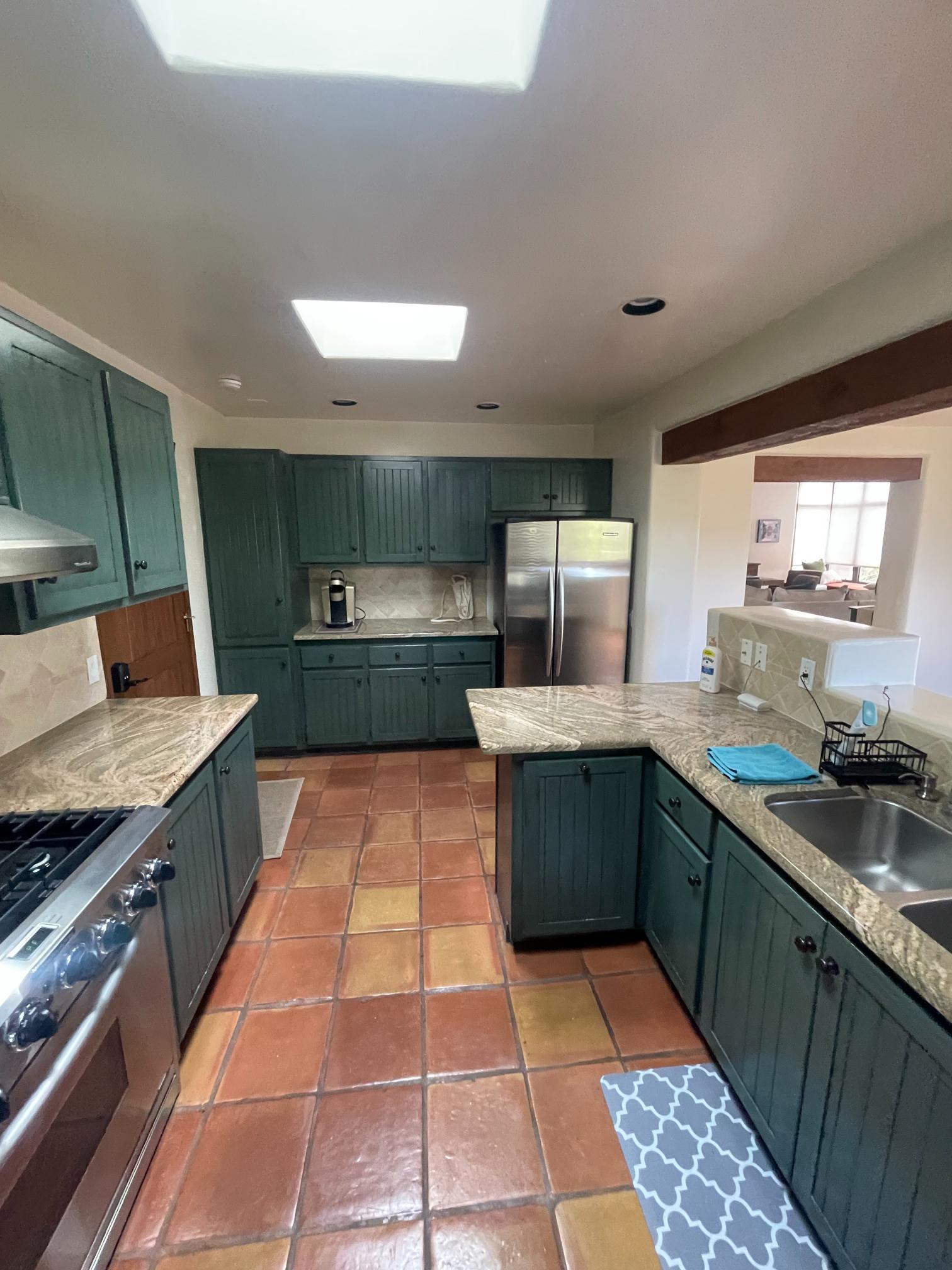 Spacious kitchen with green cabinets and terracotta tile flooring.