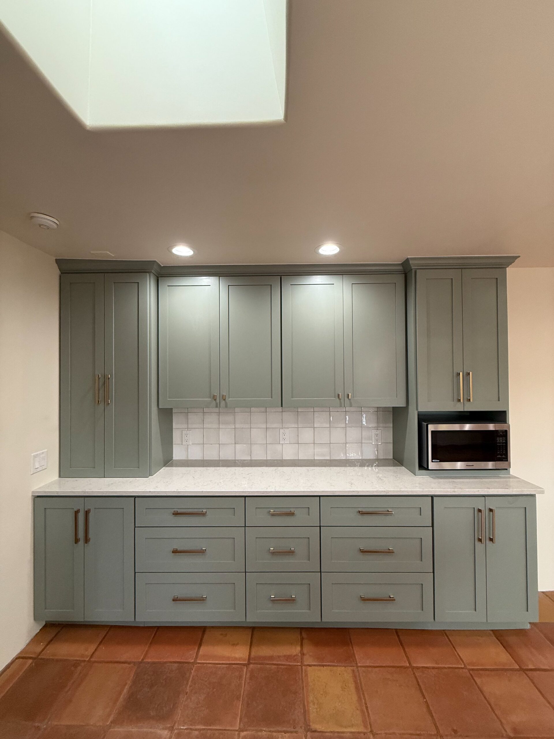 Modern kitchen cabinets with greenish-gray finish and white tiled backsplash.