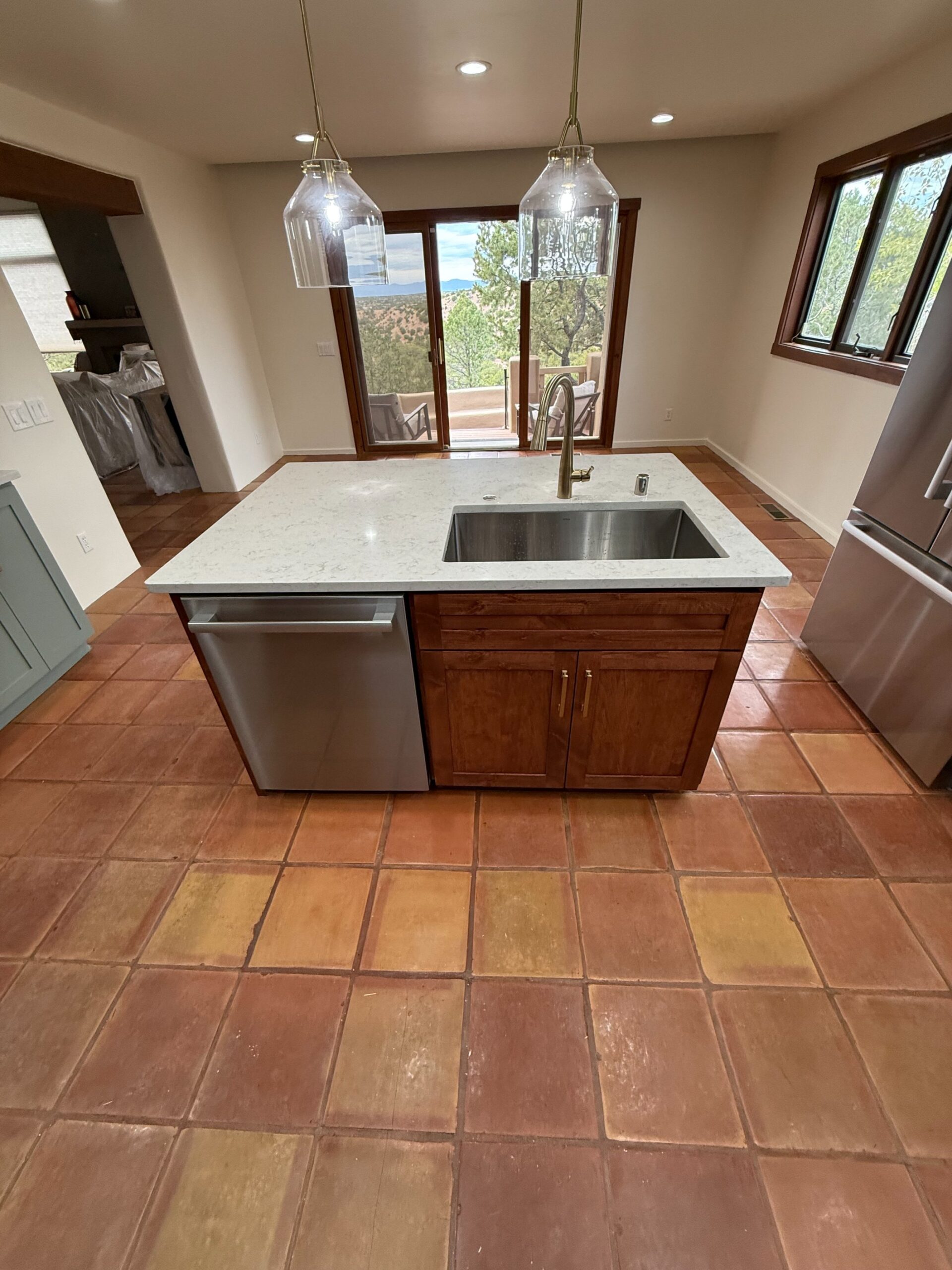 Modern kitchen island with sink and stainless dishwasher on terracotta tile floor.