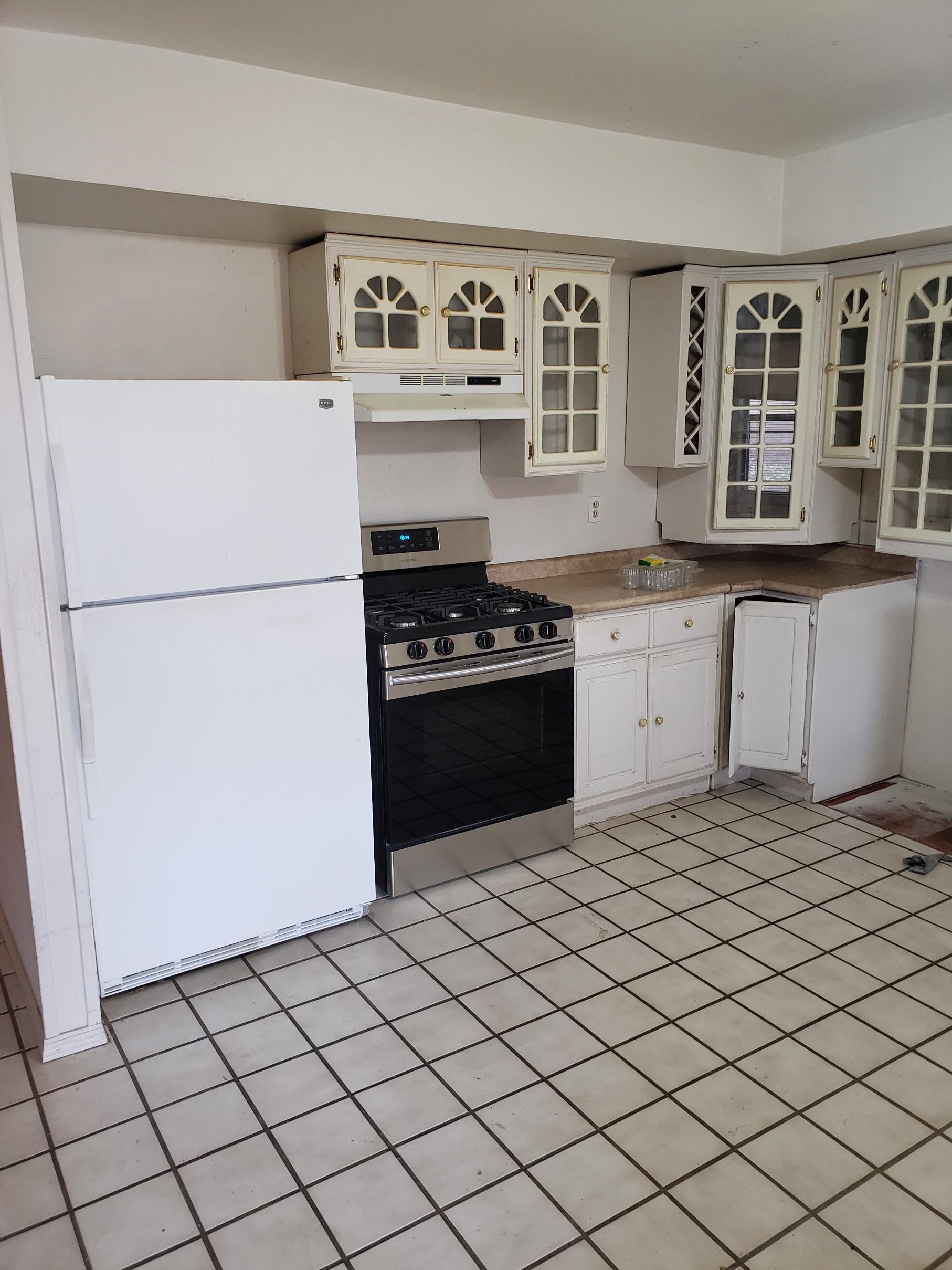 Old kitchen with white appliances and tiled floor.