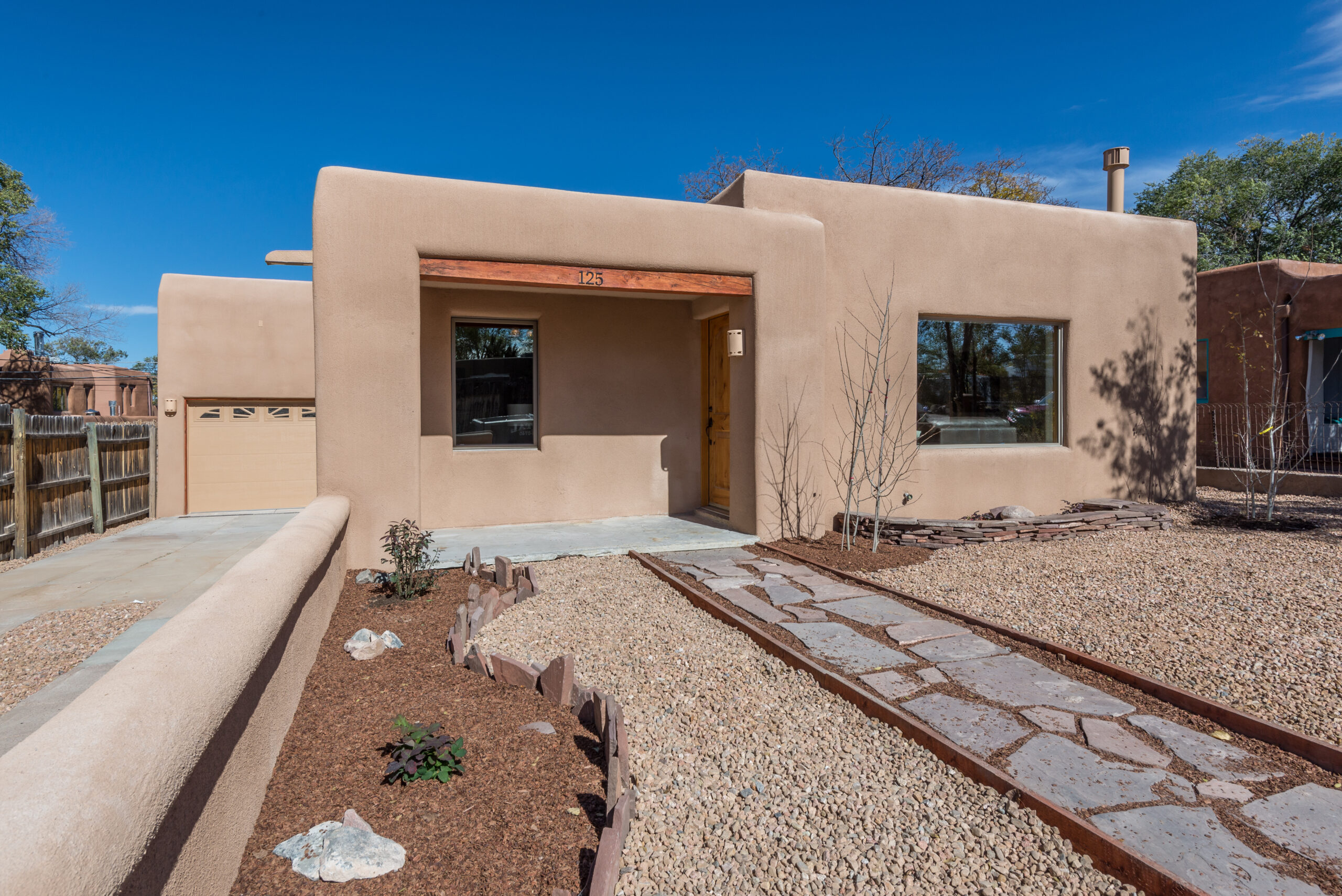 Newly constructed adobe-style home with desert landscaping and stone pathway.