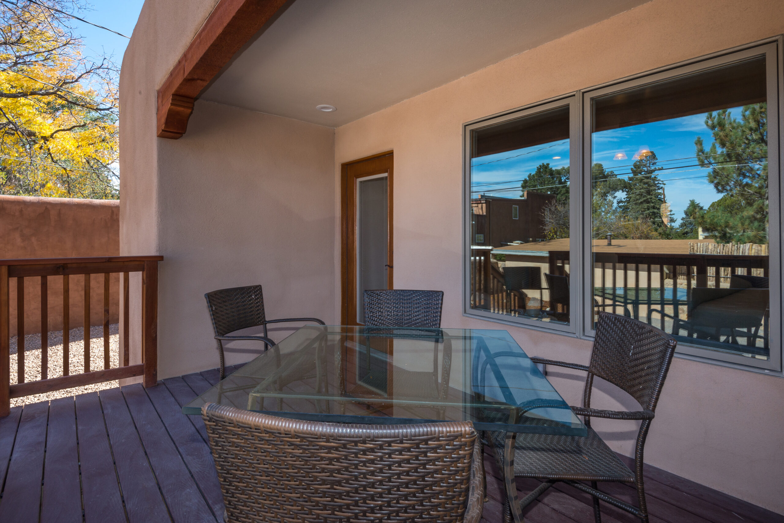 Outdoor patio with glass table and wicker chairs under a covered roof.