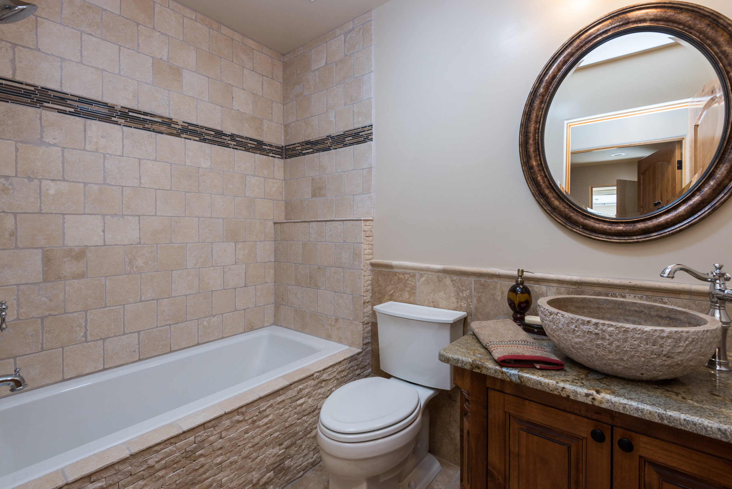 Cozy bathroom with stone-tiled walls, bathtub, toilet, and wooden vanity.