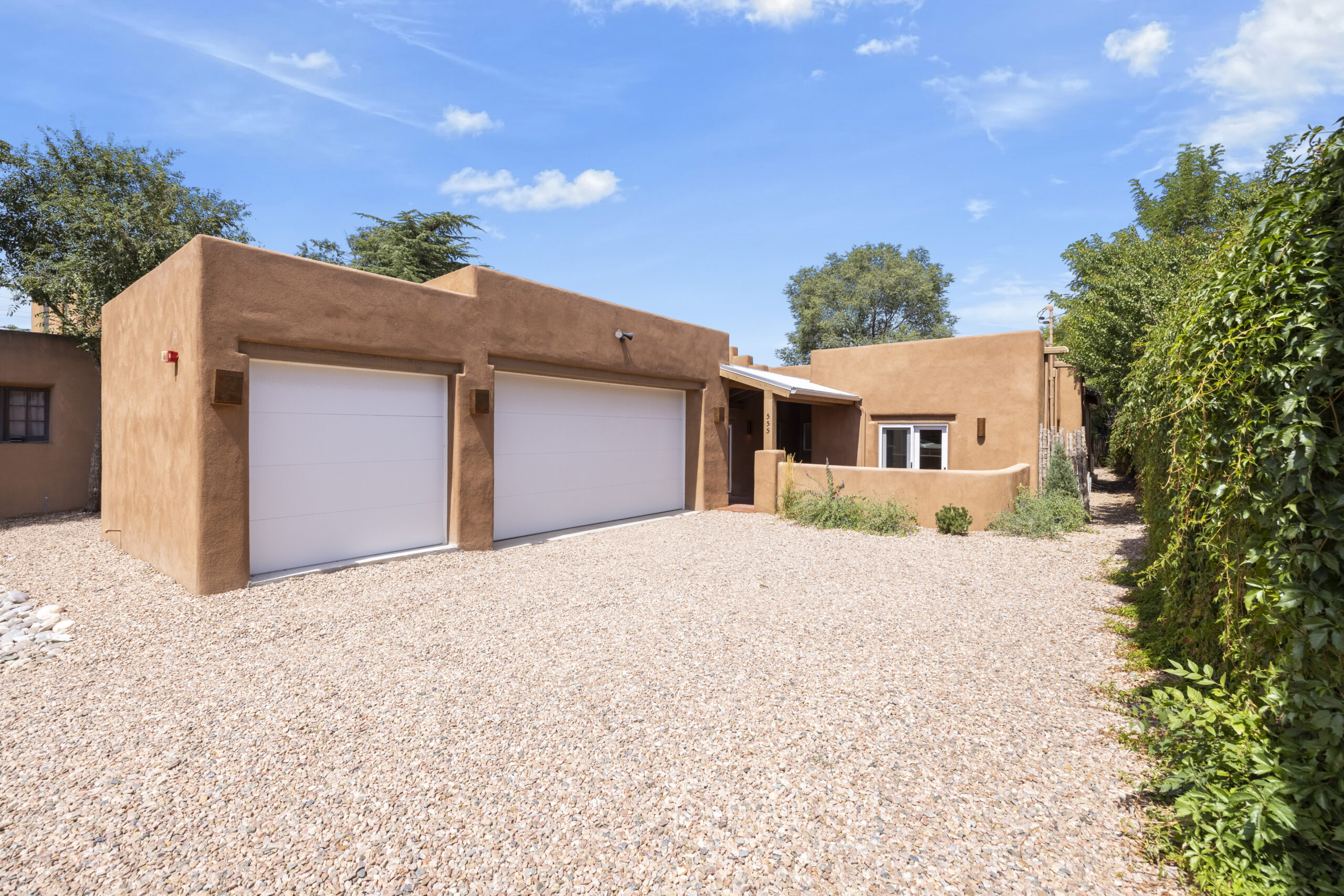 Modern adobe-style house with two-car garage and gravel driveway.