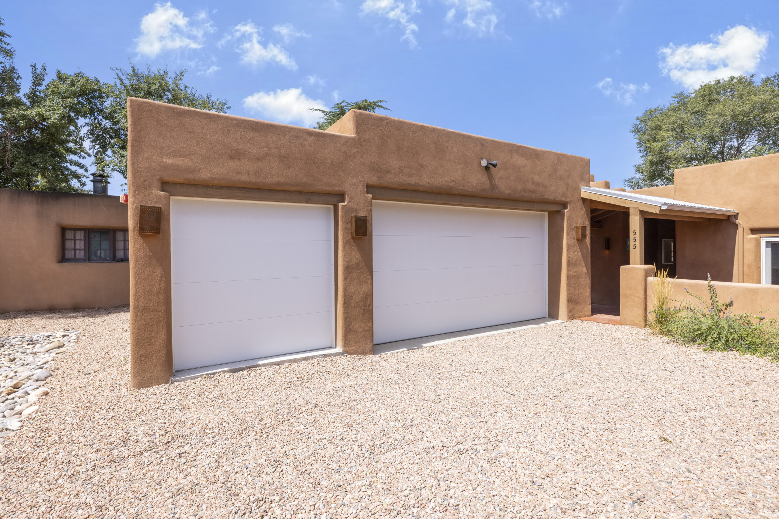 Two white garage doors on a beige stucco house with gravel driveway.