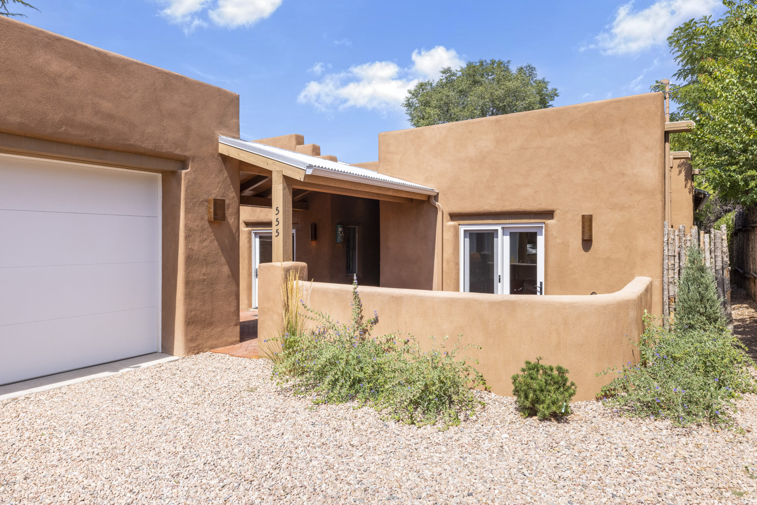 Southwestern style adobe home with a gravel driveway and blue sky.
