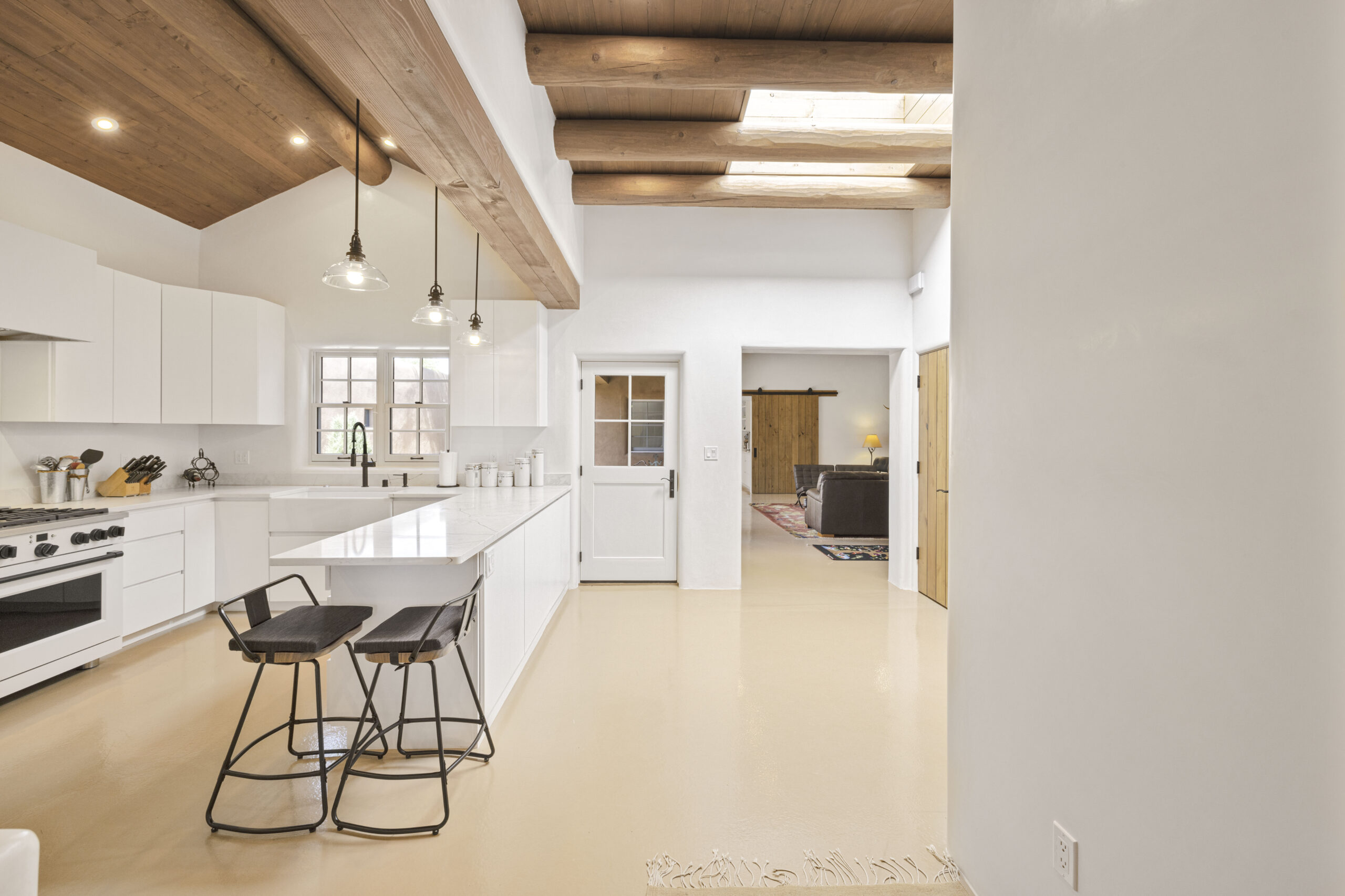 Modern kitchen with white cabinets and wooden ceiling beams.
