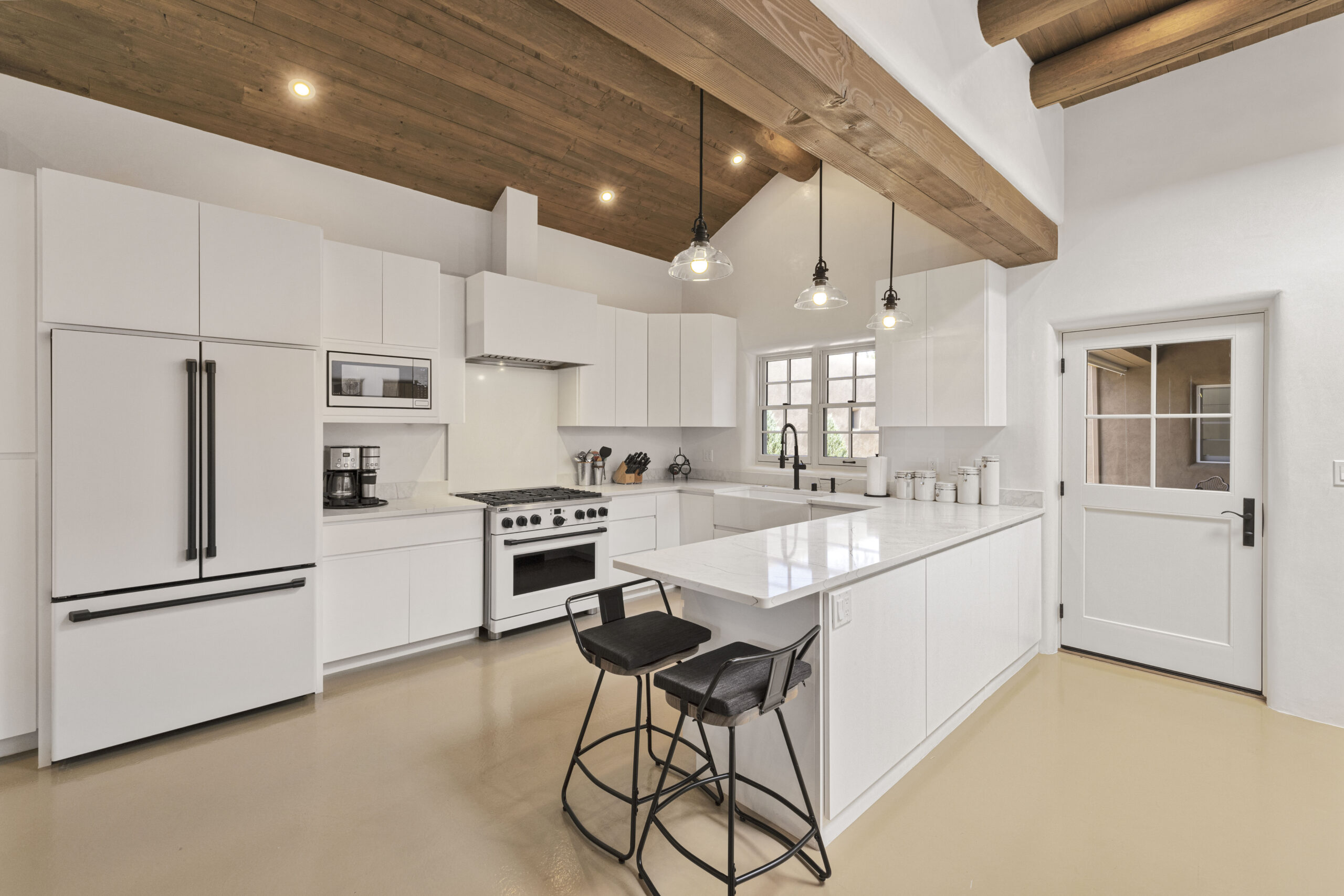 Modern white kitchen with wooden ceiling beams and island seating.