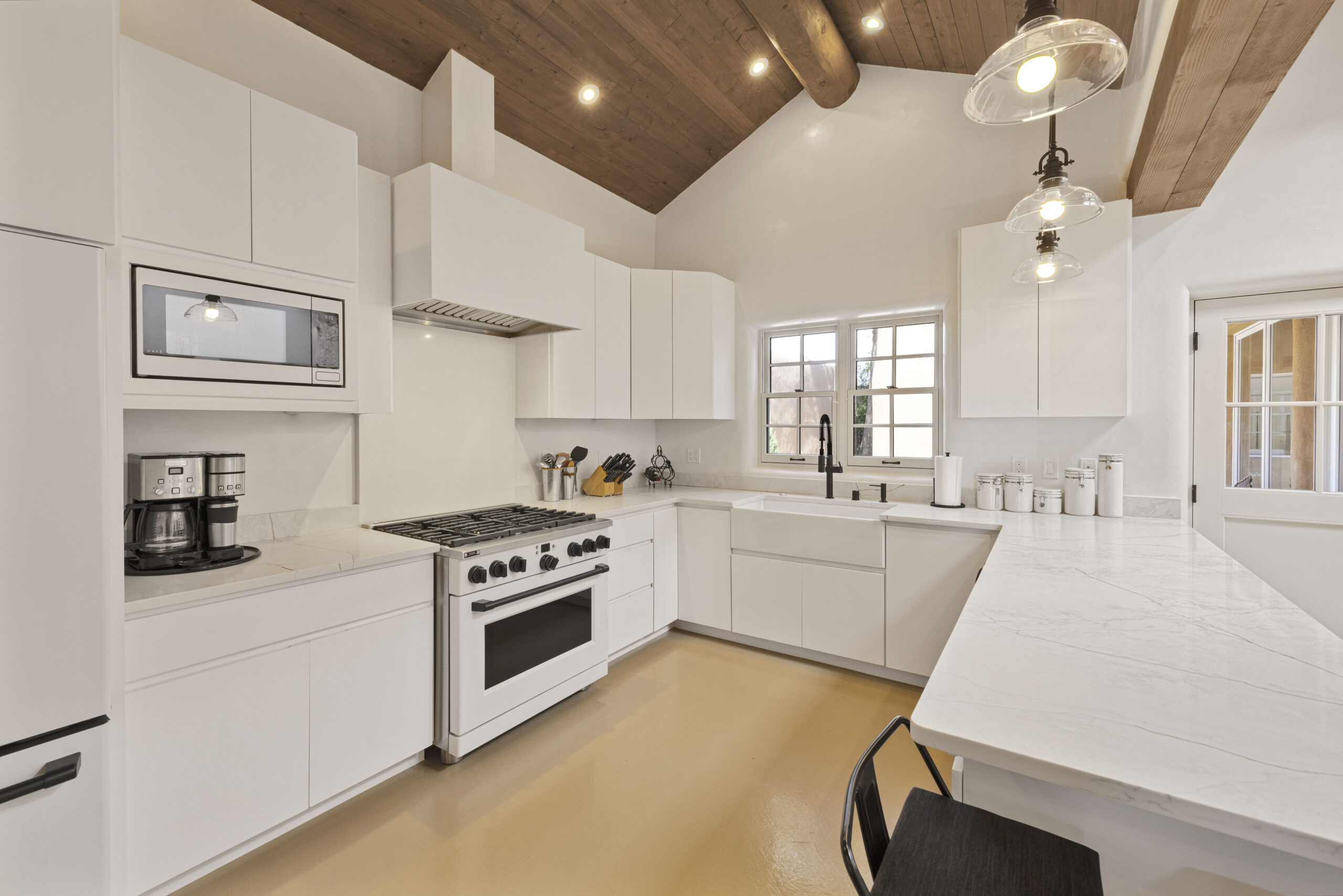 Bright modern kitchen with white cabinetry and wooden ceiling beams.