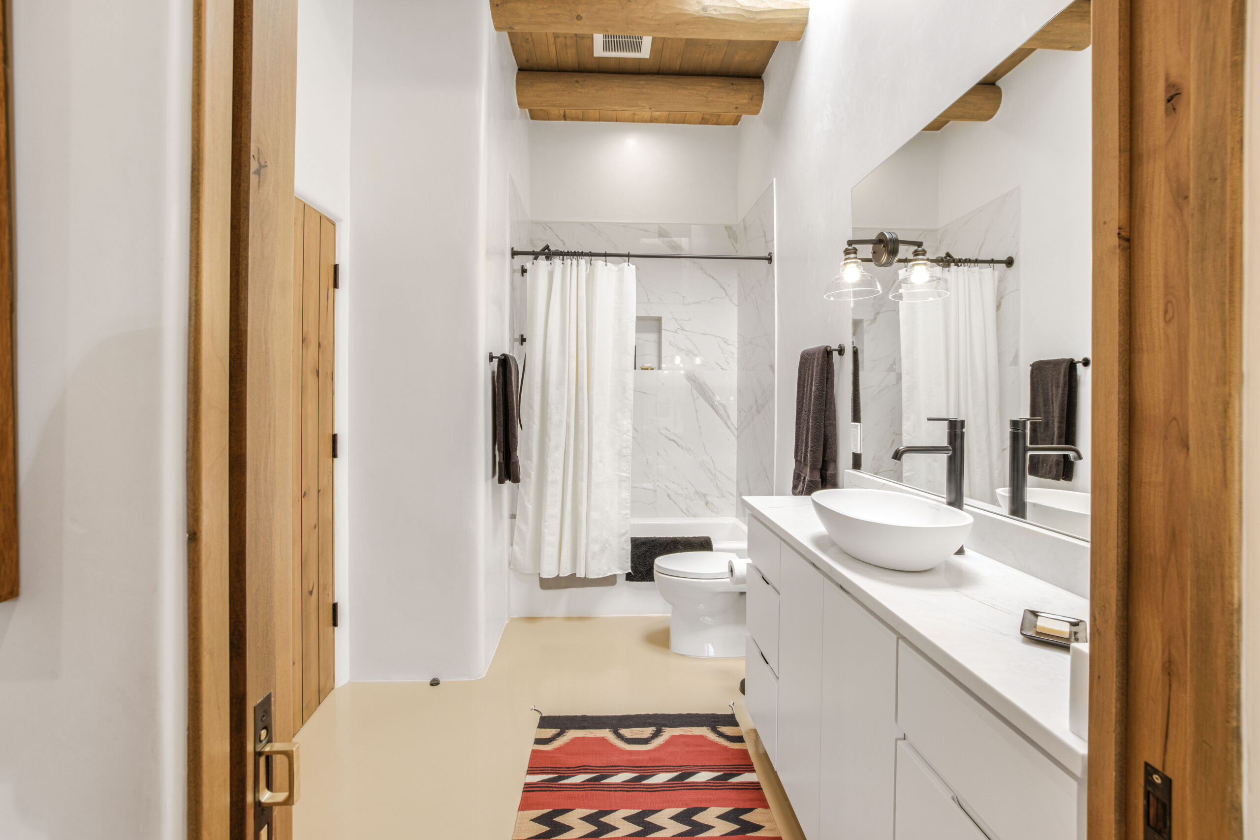 Bright bathroom with white walls, wooden accents, and a colorful rug.