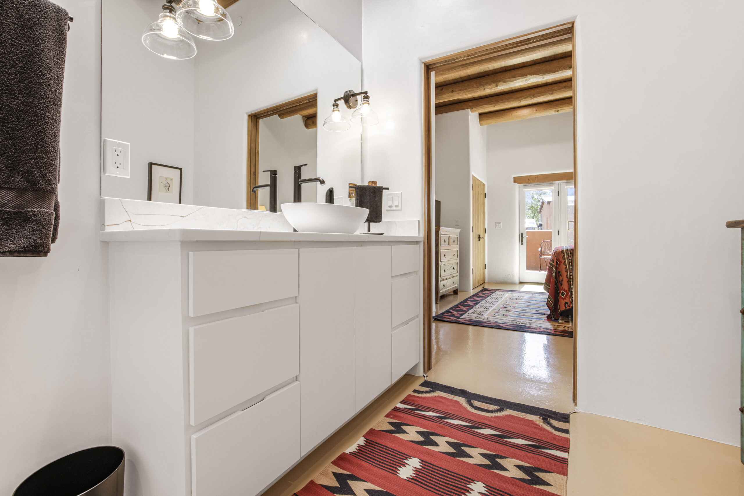 Modern white bathroom vanity with a colorful rug and wooden accents.