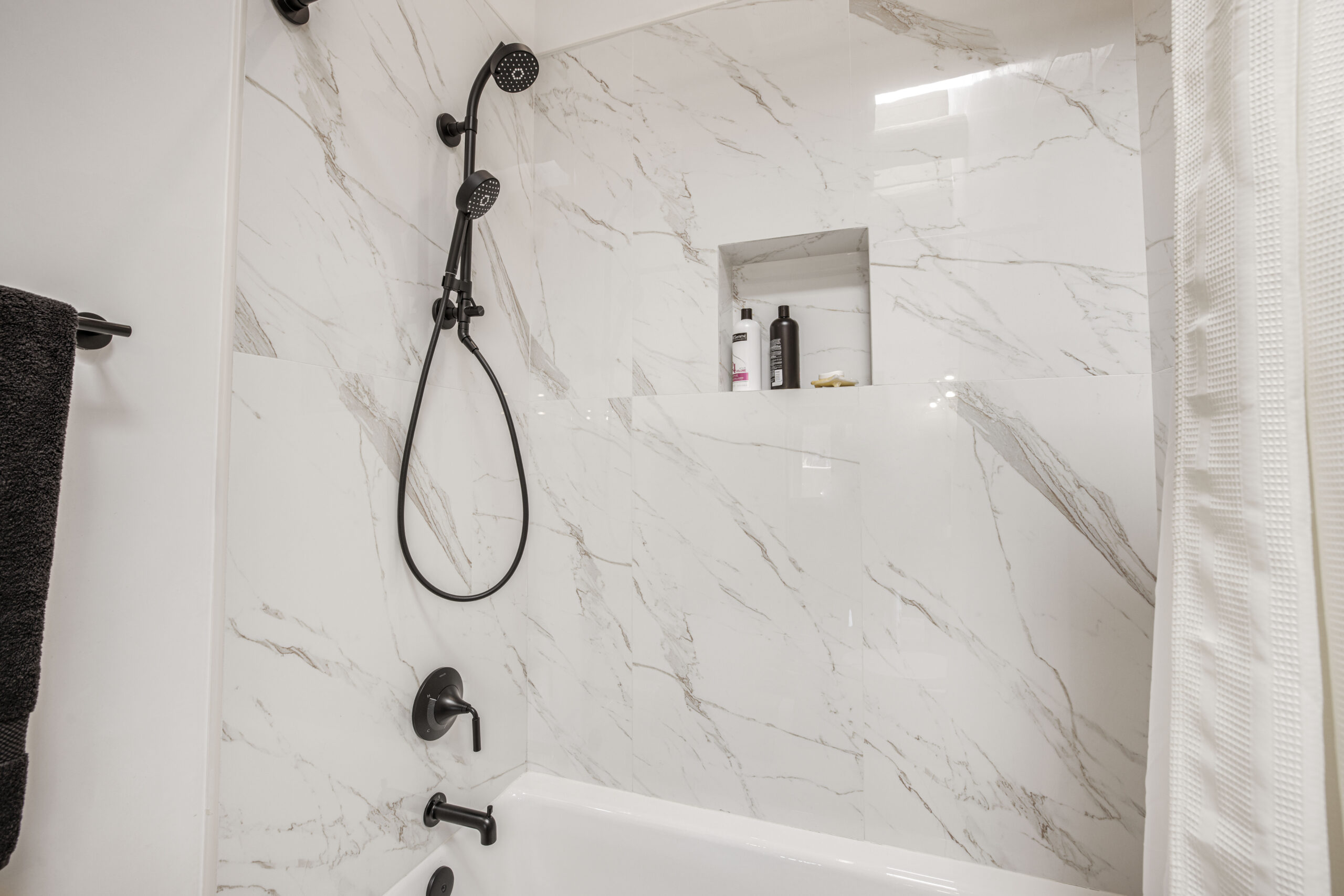 Modern bathroom with marble walls and black shower fixtures.