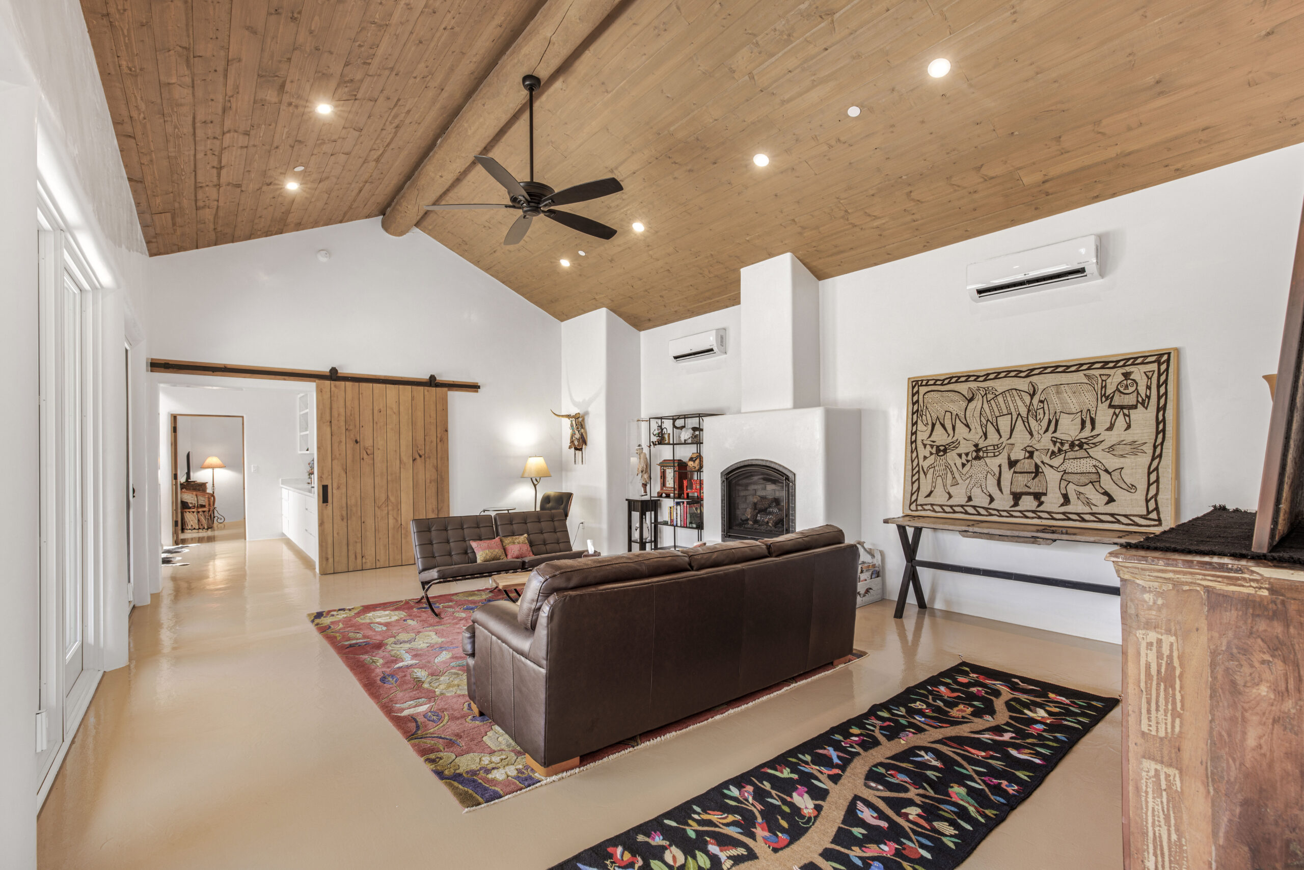 Spacious living room with leather sofas, rugs, and a ceiling fan under exposed wooden beams.