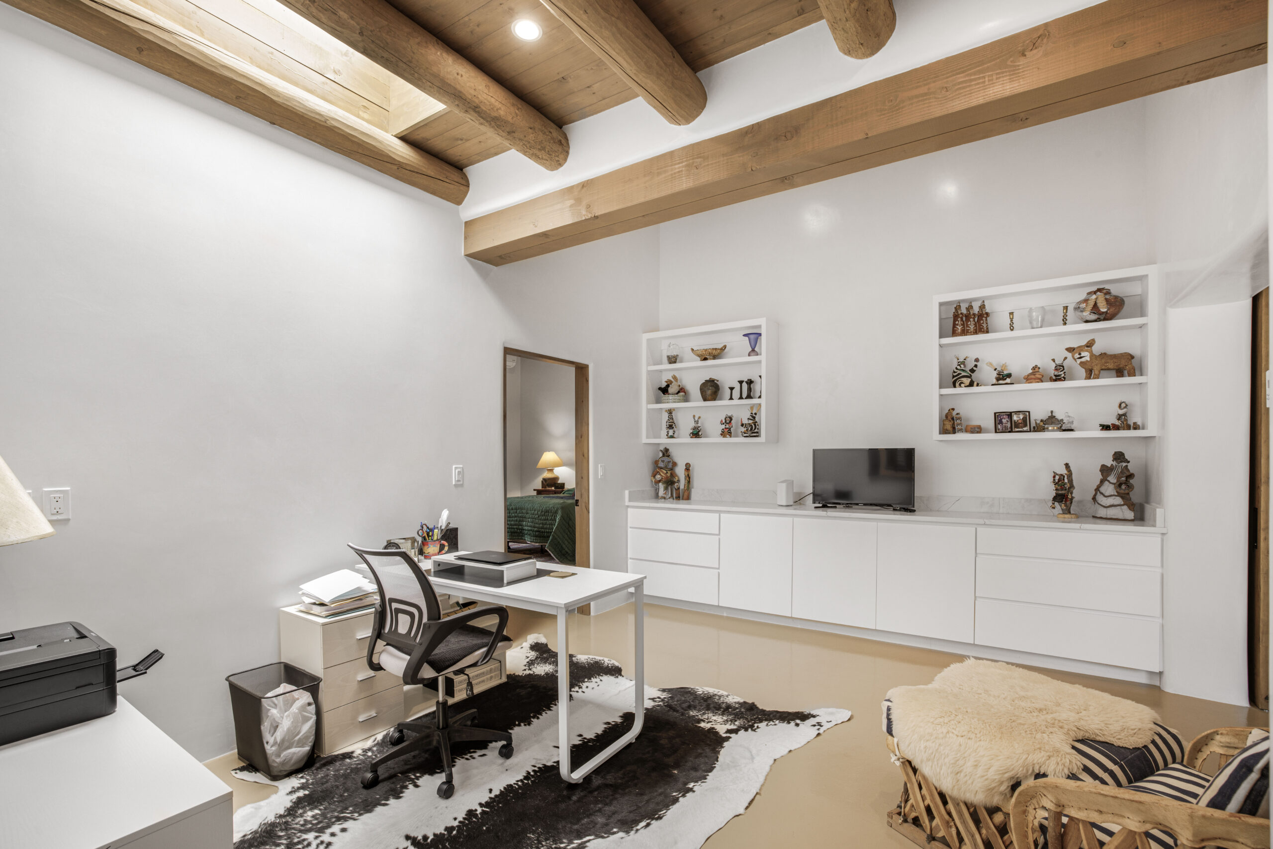 Modern home office with white walls and wooden ceiling beams.