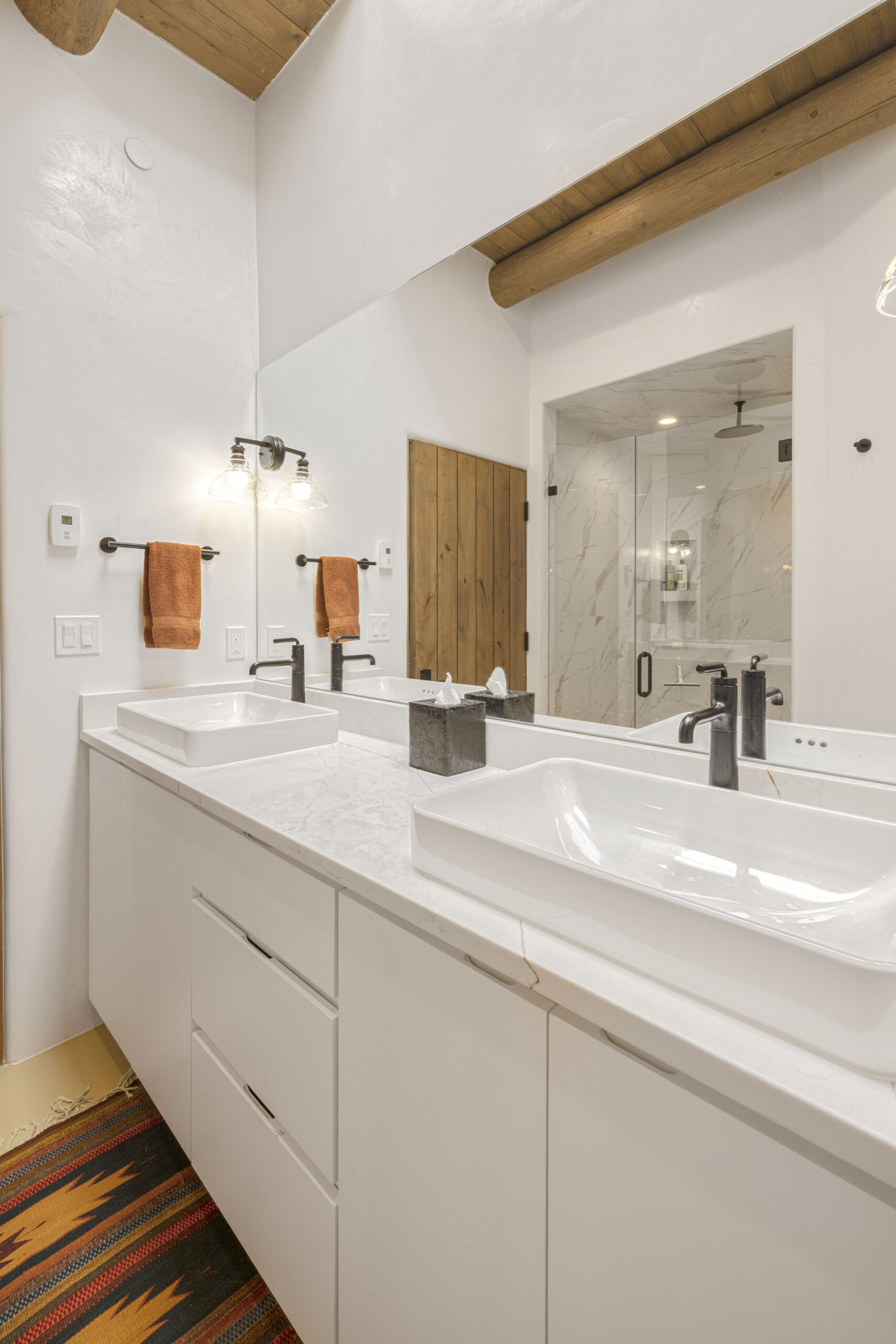 Modern bathroom with double sinks, large mirror, and glass shower enclosure.