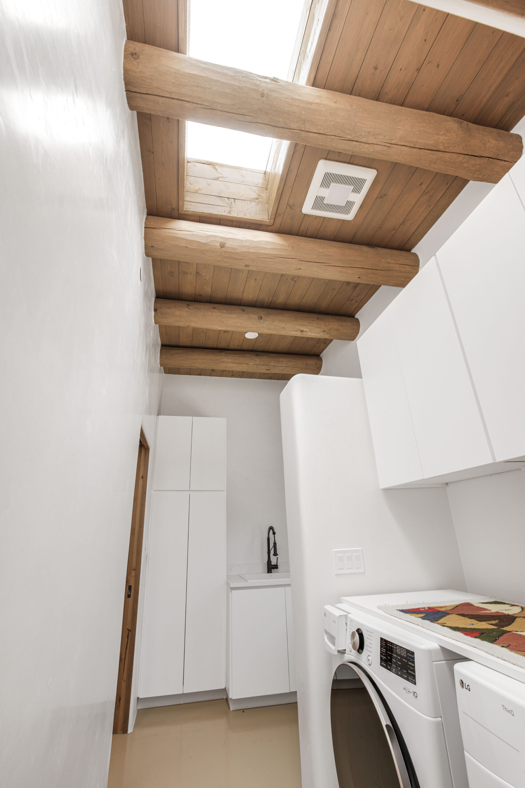 Minimalist kitchen with wooden ceiling beams and white cabinetry.